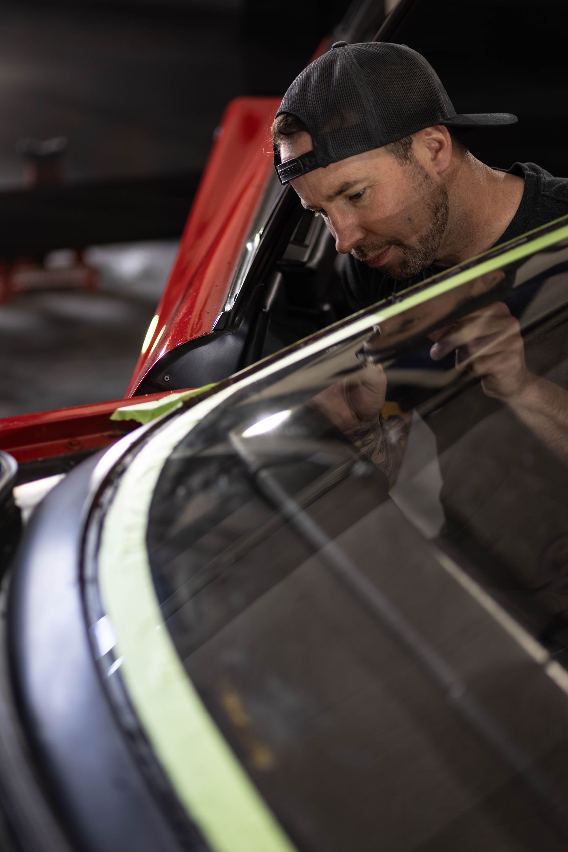 Mechanic working on a car under an open hood in a dim garage