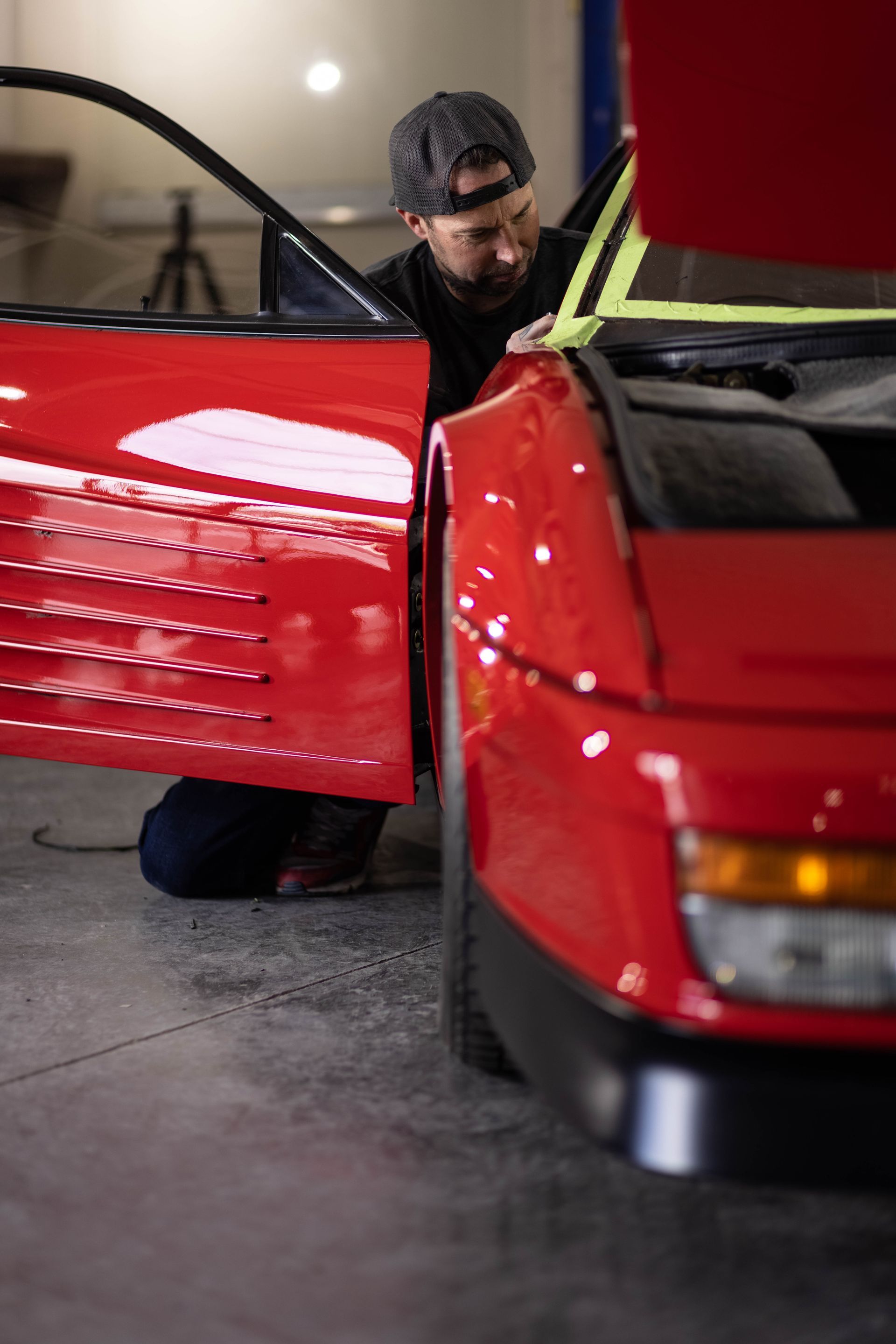 Mechanic inspecting a red sports car with the hood open in a garage