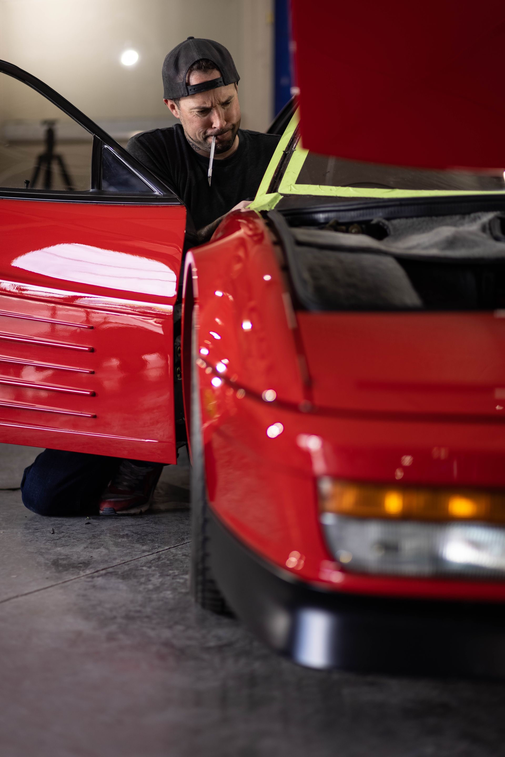 Mechanic inspecting a red car with the hood and door open in a garage