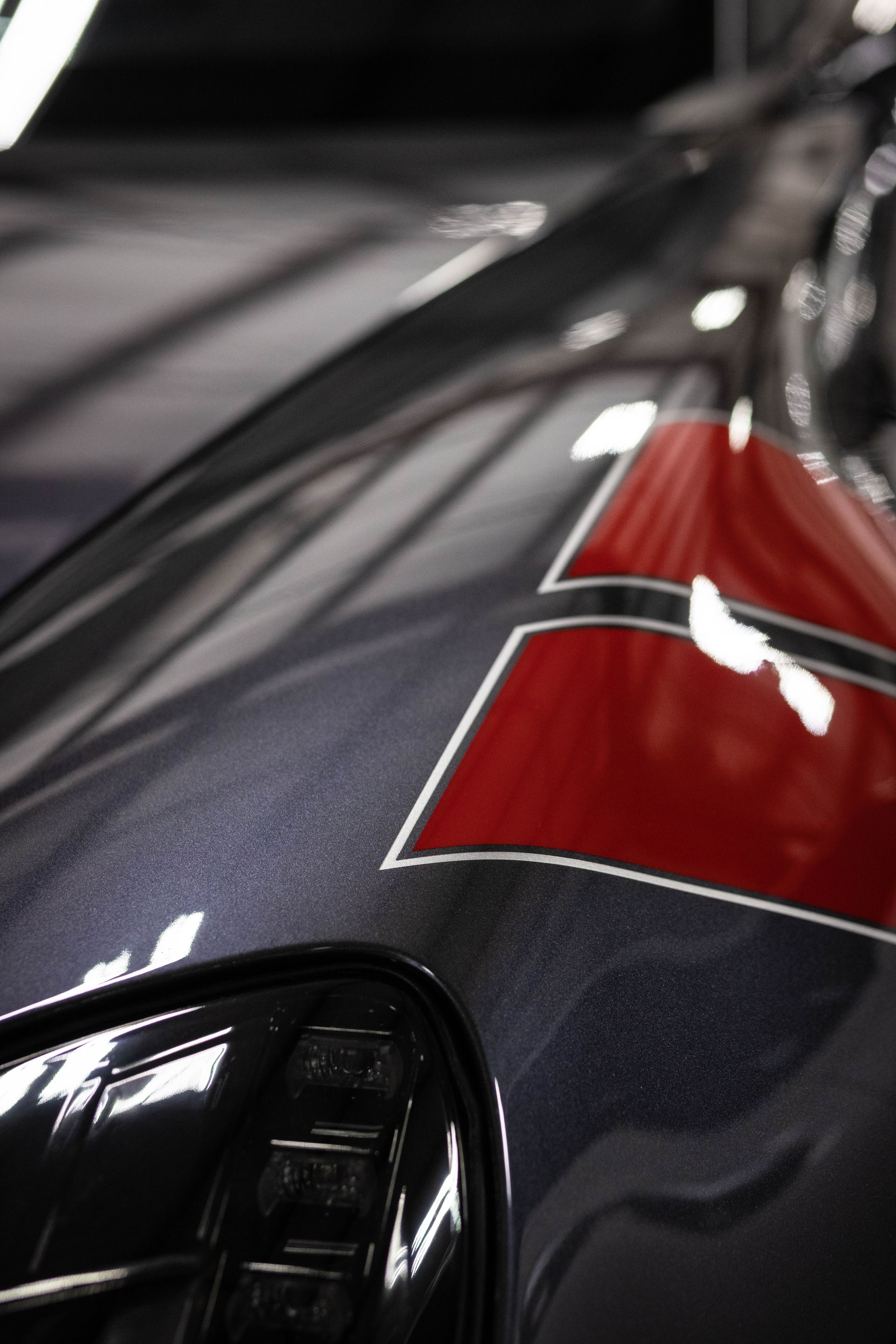 Close-up of a glossy dark car hood with a red stripe and chrome trim.