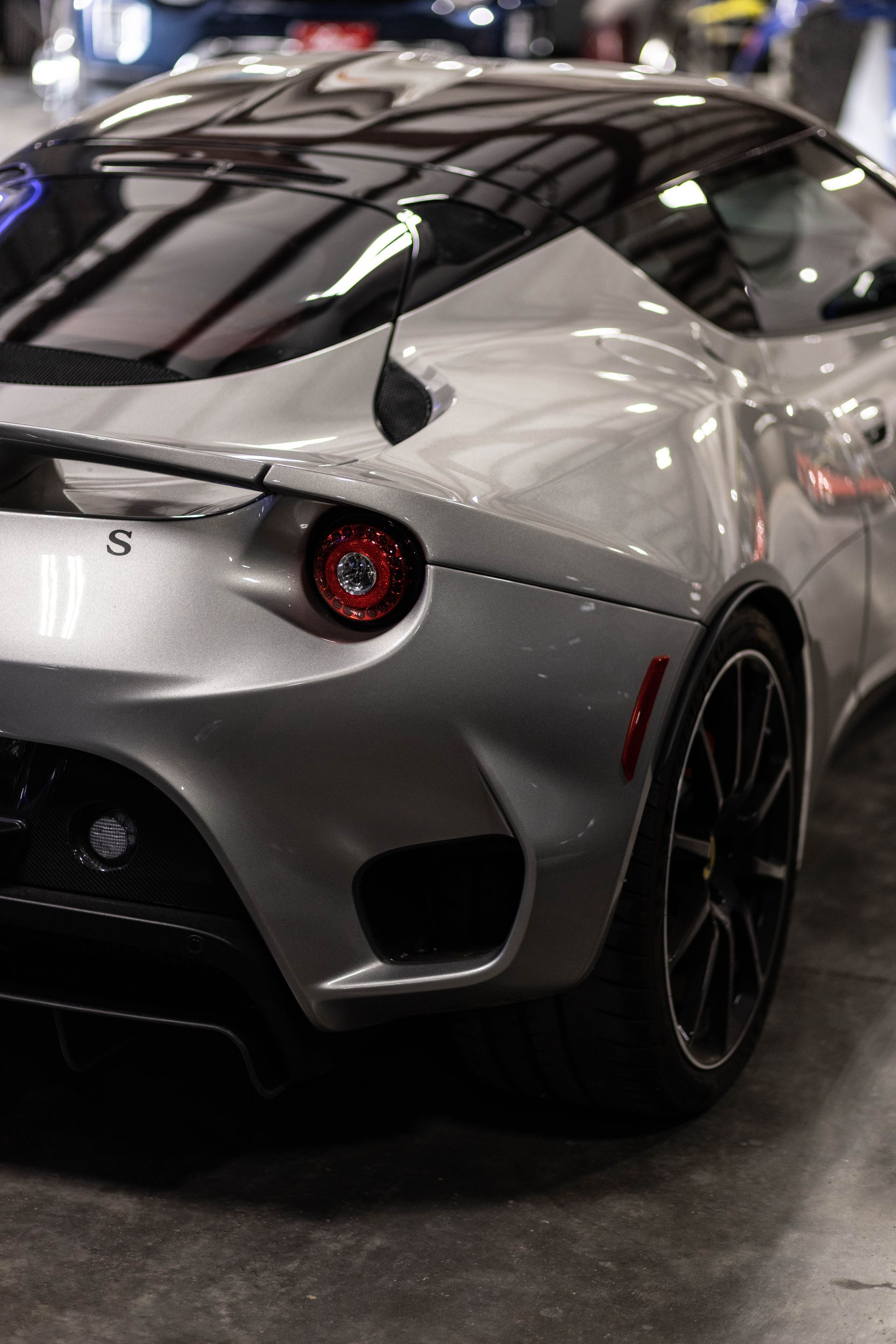 Silver sports car rear view at an auto show, with red taillight and black racing wheels