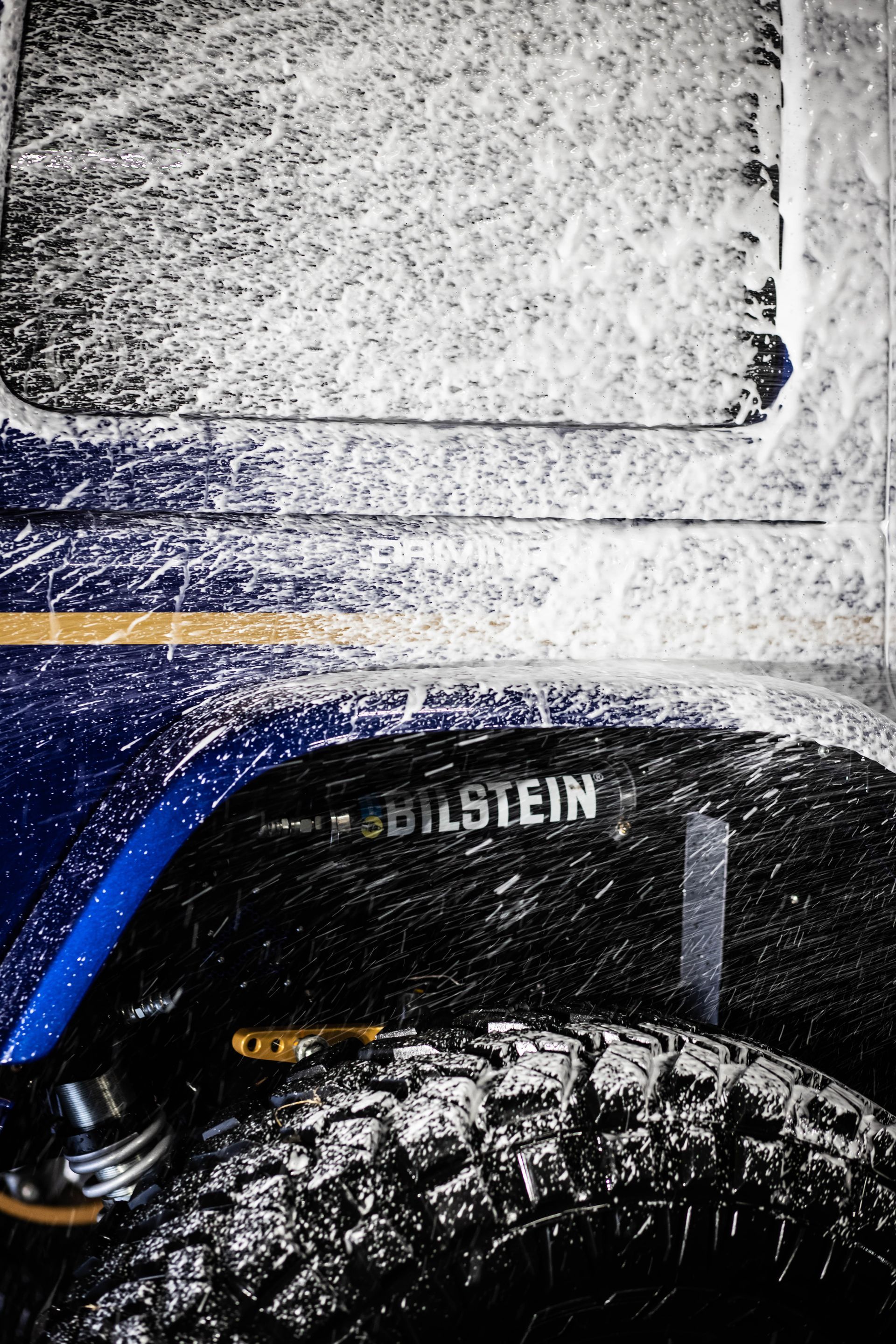 Blue off-road vehicle wheel and fender covered in mud and snow, with Bilstein suspension visible