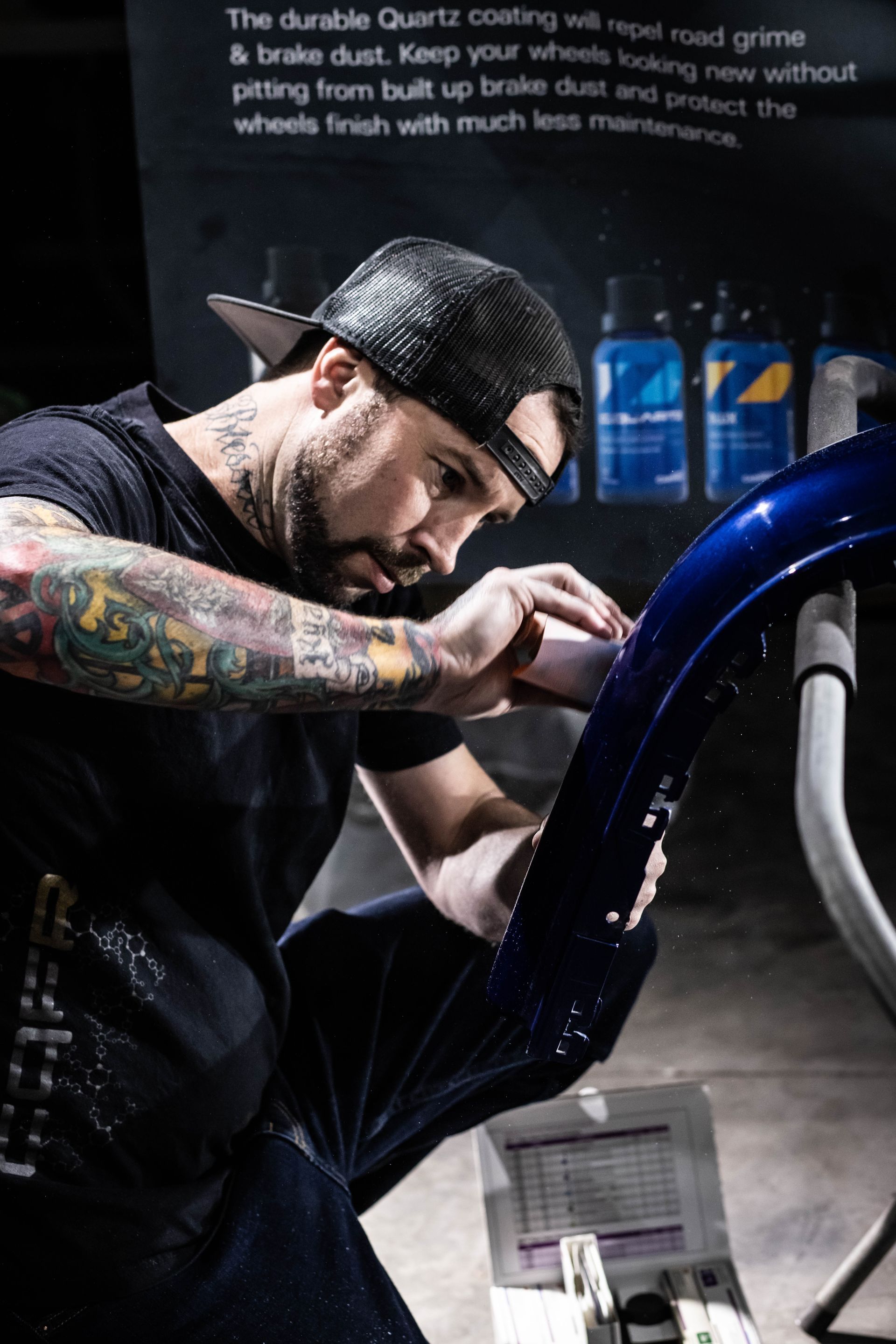 Tattooed mechanic repairing a blue car in a dim garage, focused on work