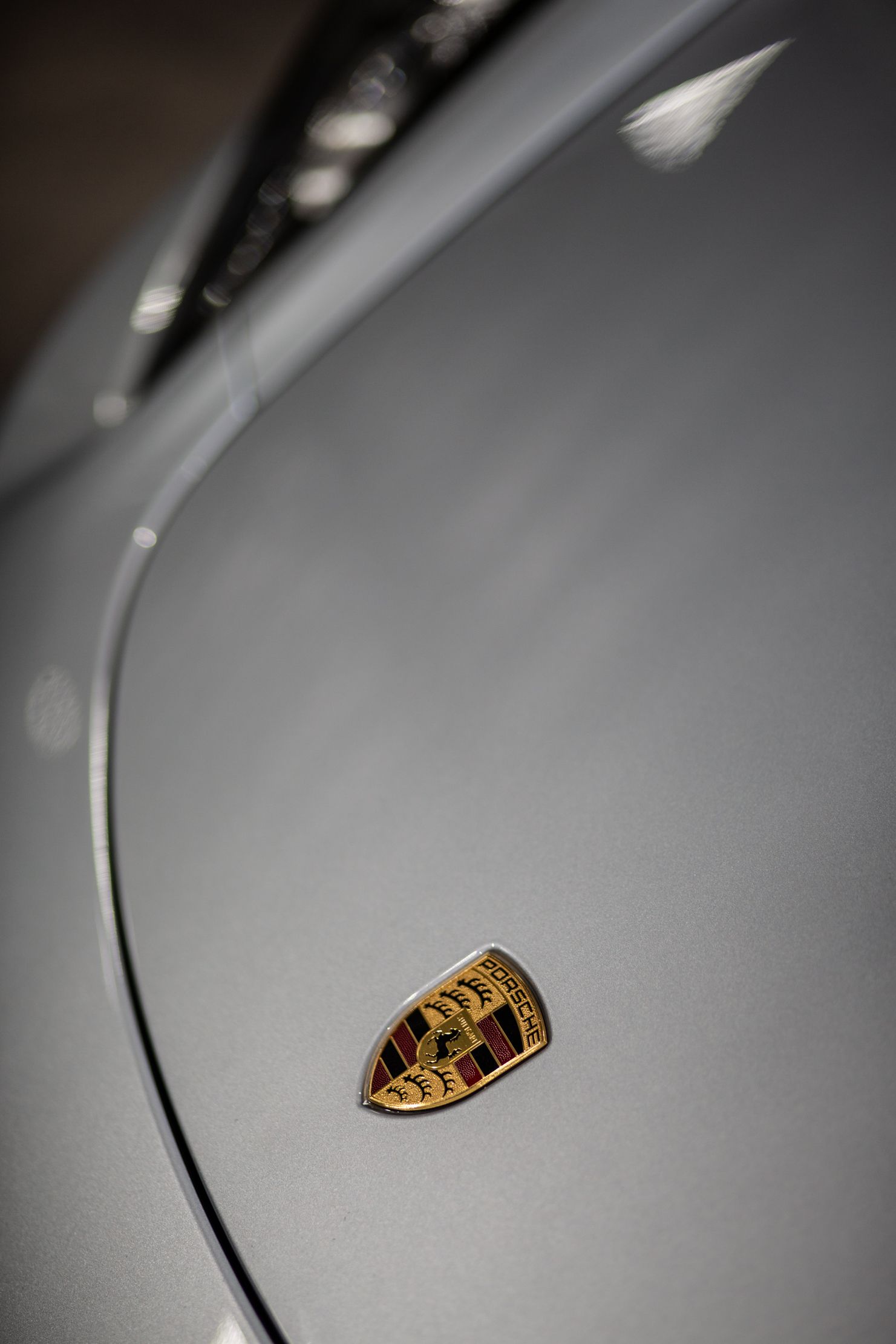 Close-up of a Porsche hood emblem on a silver car