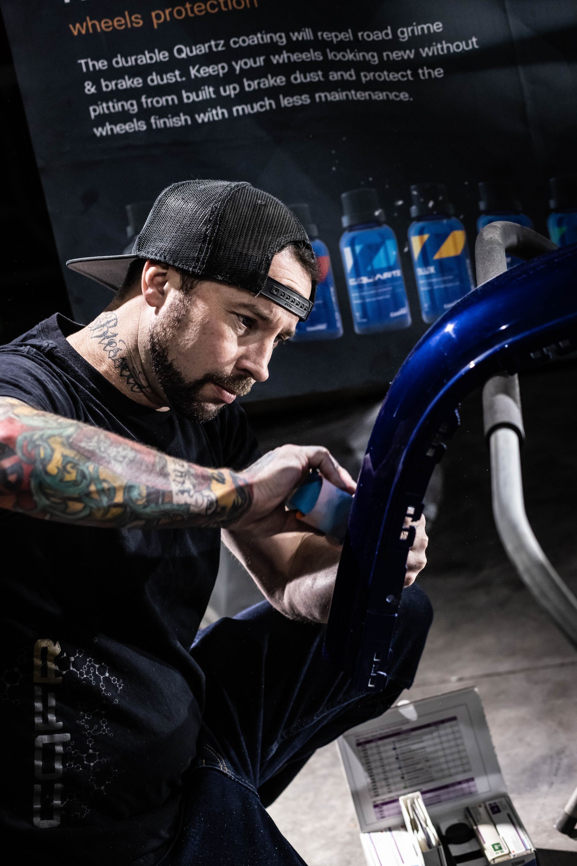 Mechanic polishing a blue car in a dim garage, focused on detailing work