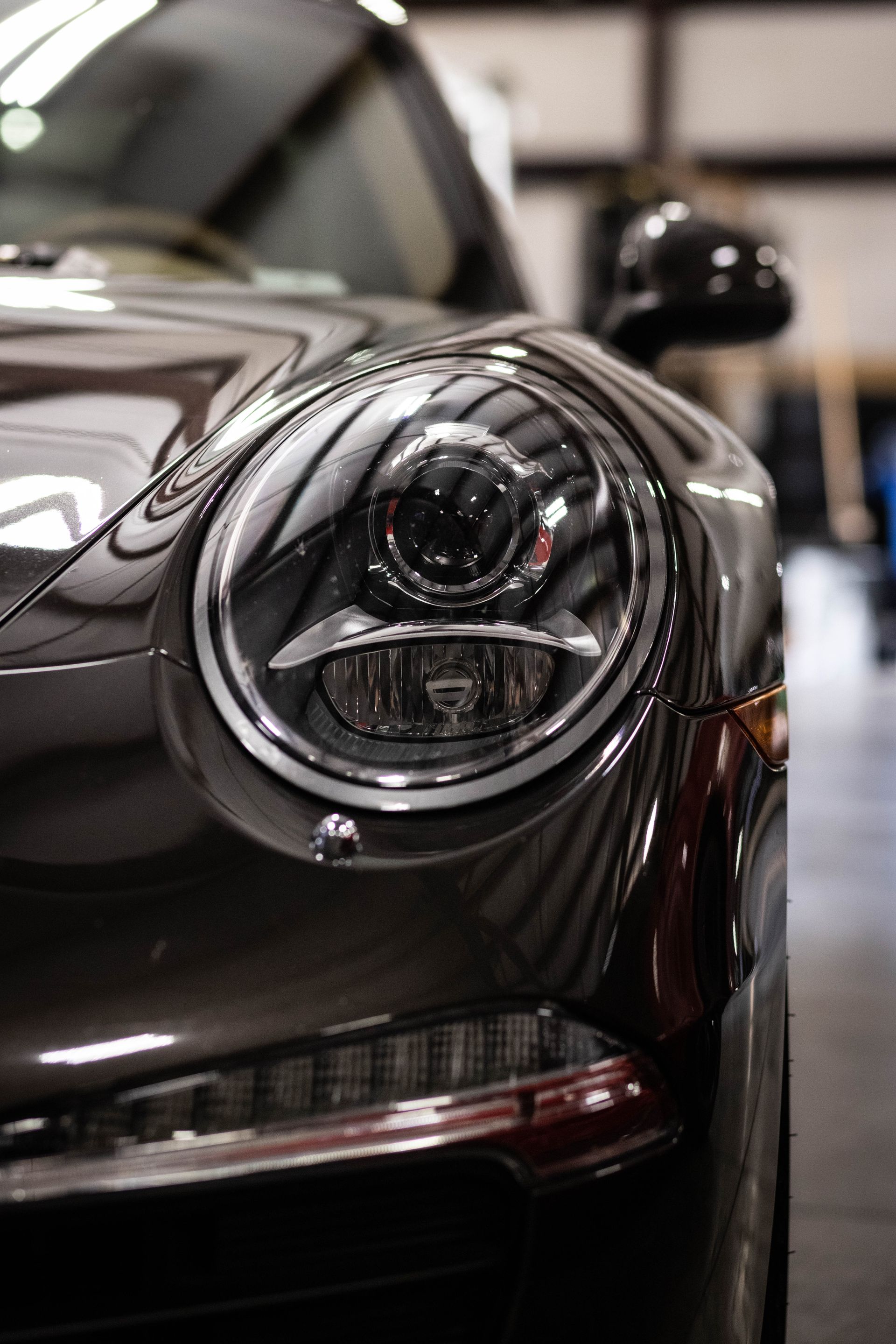 Close-up of a black sports car’s headlight and glossy front fender in a showroom