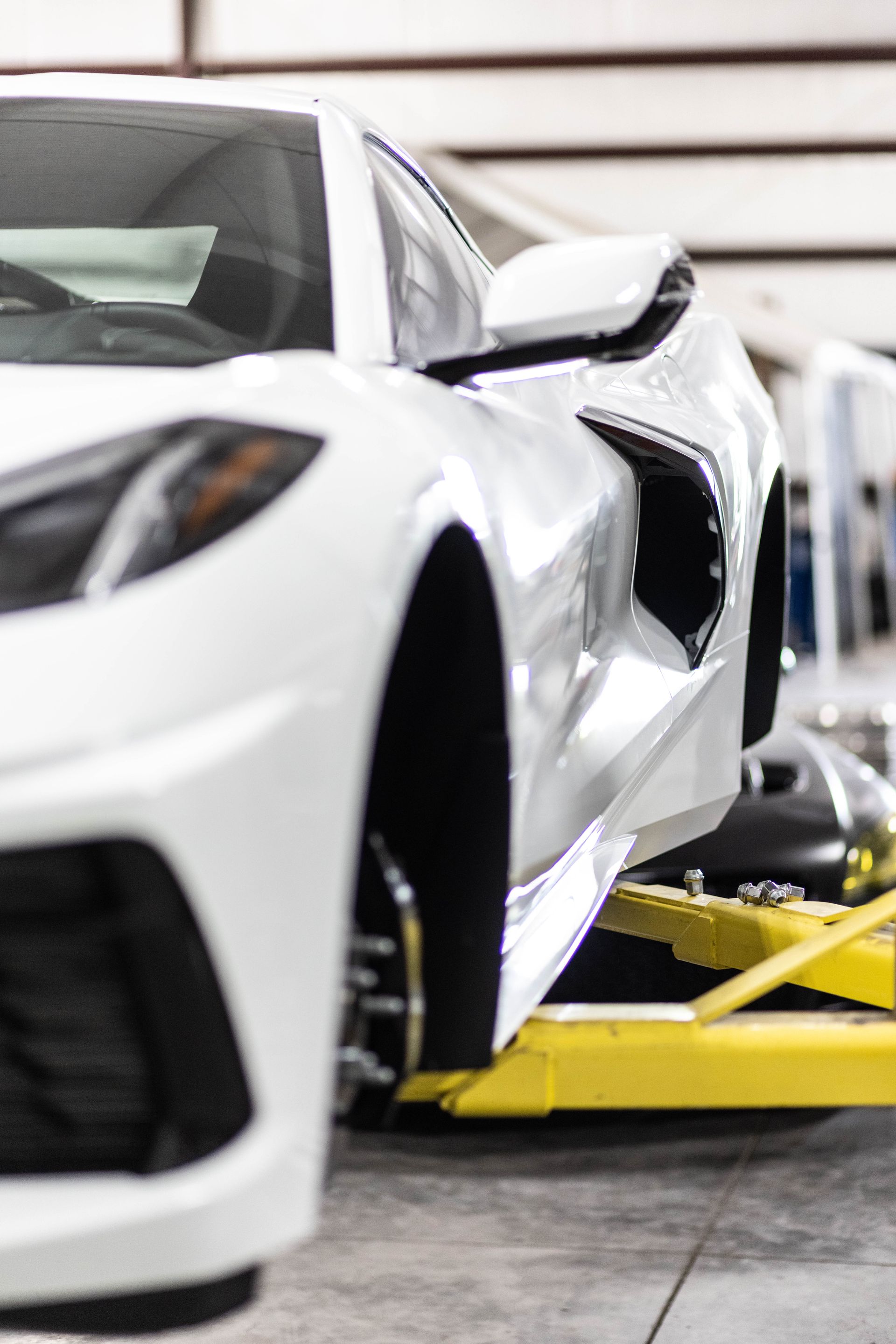 White sports car on a yellow lift in an auto workshop, viewed from the front side.