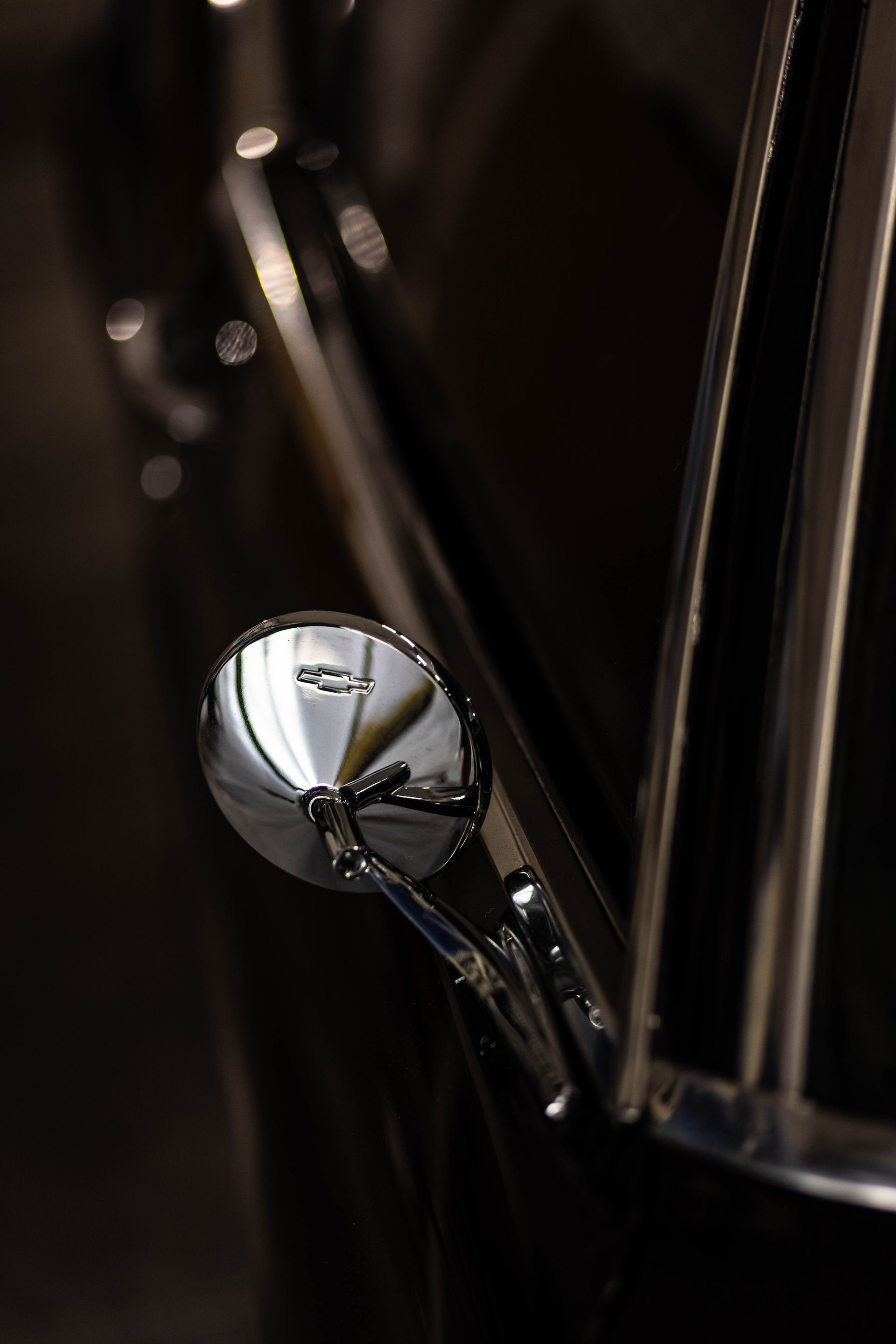 Close-up of a chrome car side mirror and glossy black body panel at night