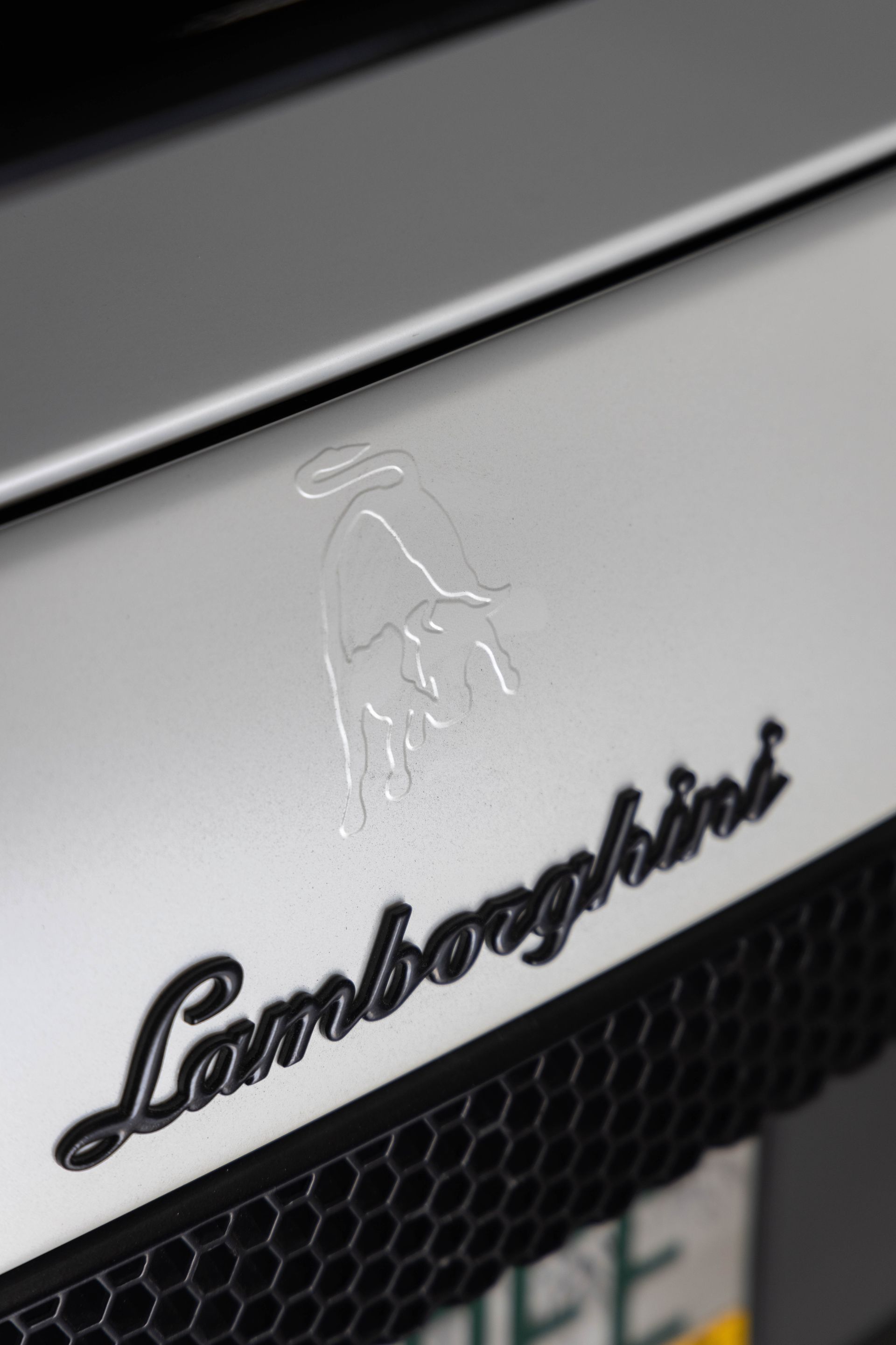 Close-up of a silver Lamborghini hood badge with the black Lamborghini script and bull emblem.