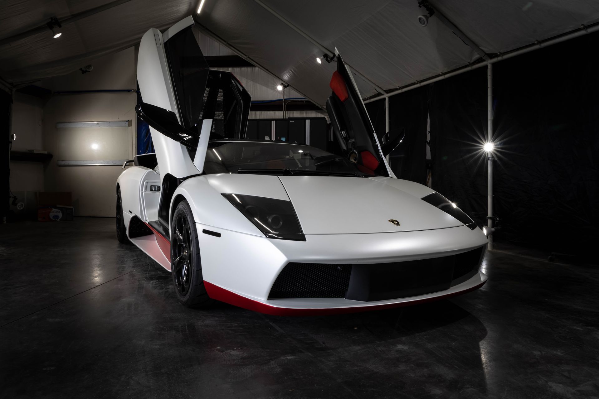 White sports car with gullwing doors open in a dark showroom, accented with red trim