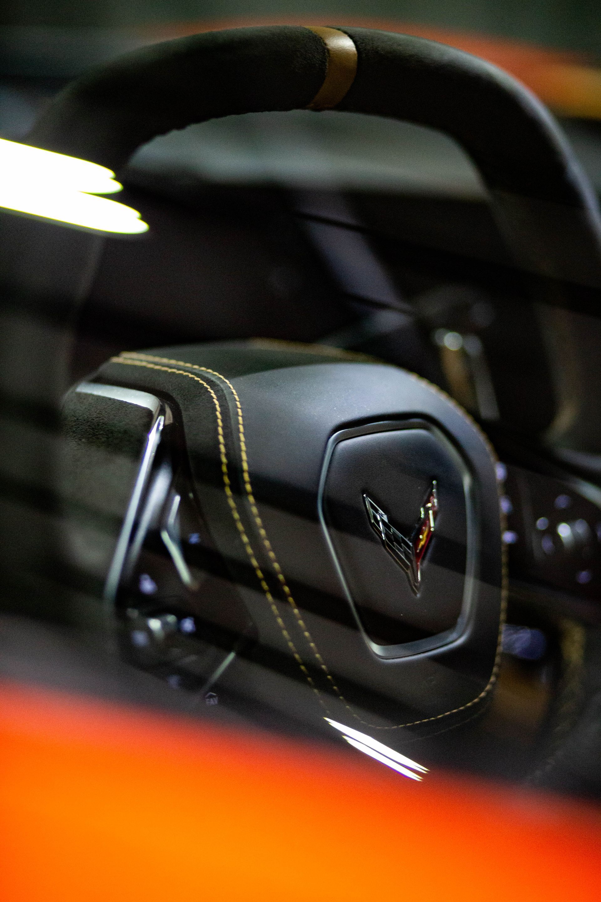 Close-up of a black car steering wheel with stitching and reflective dashboard details