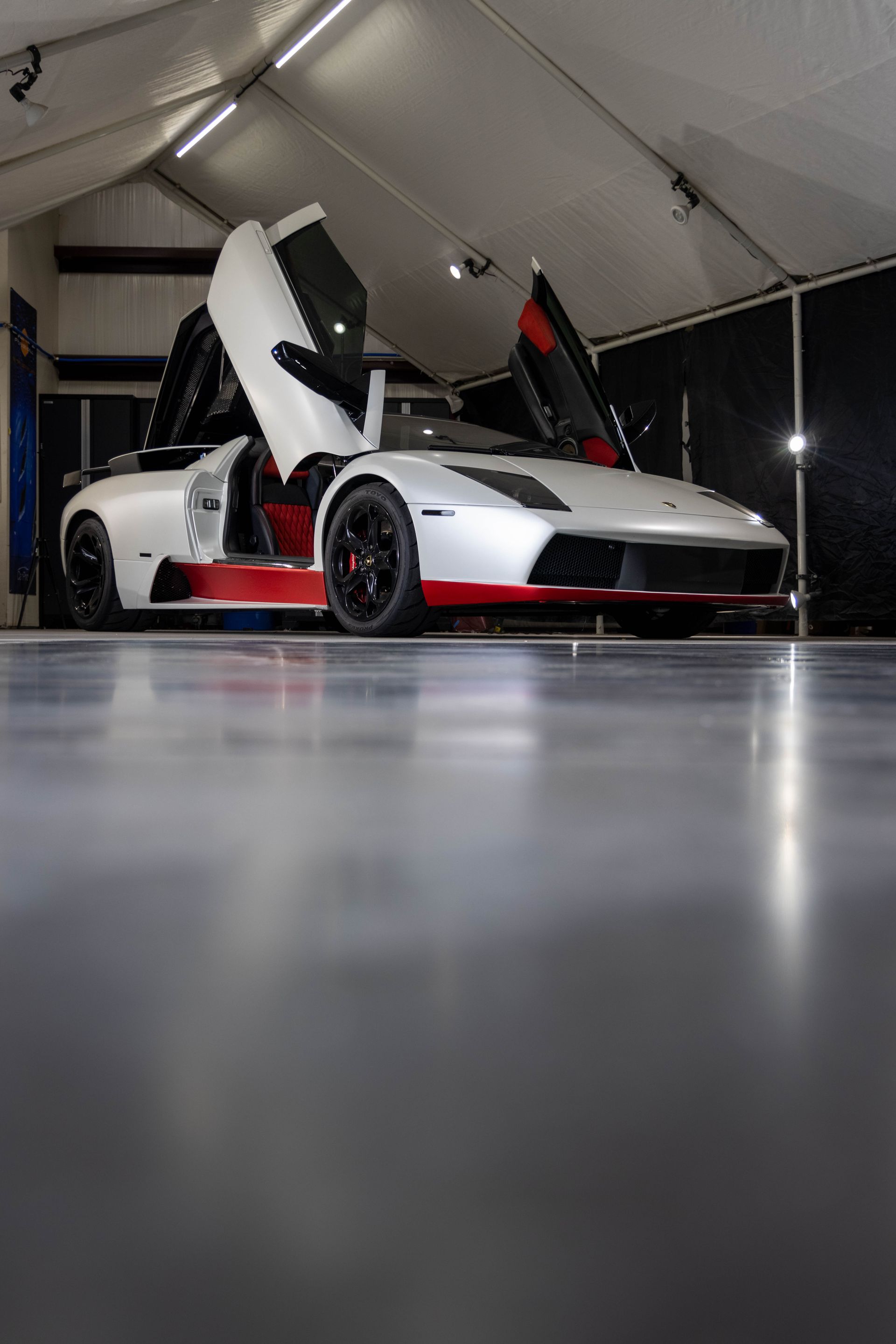 White sports car with scissor doors open inside a tented display area
