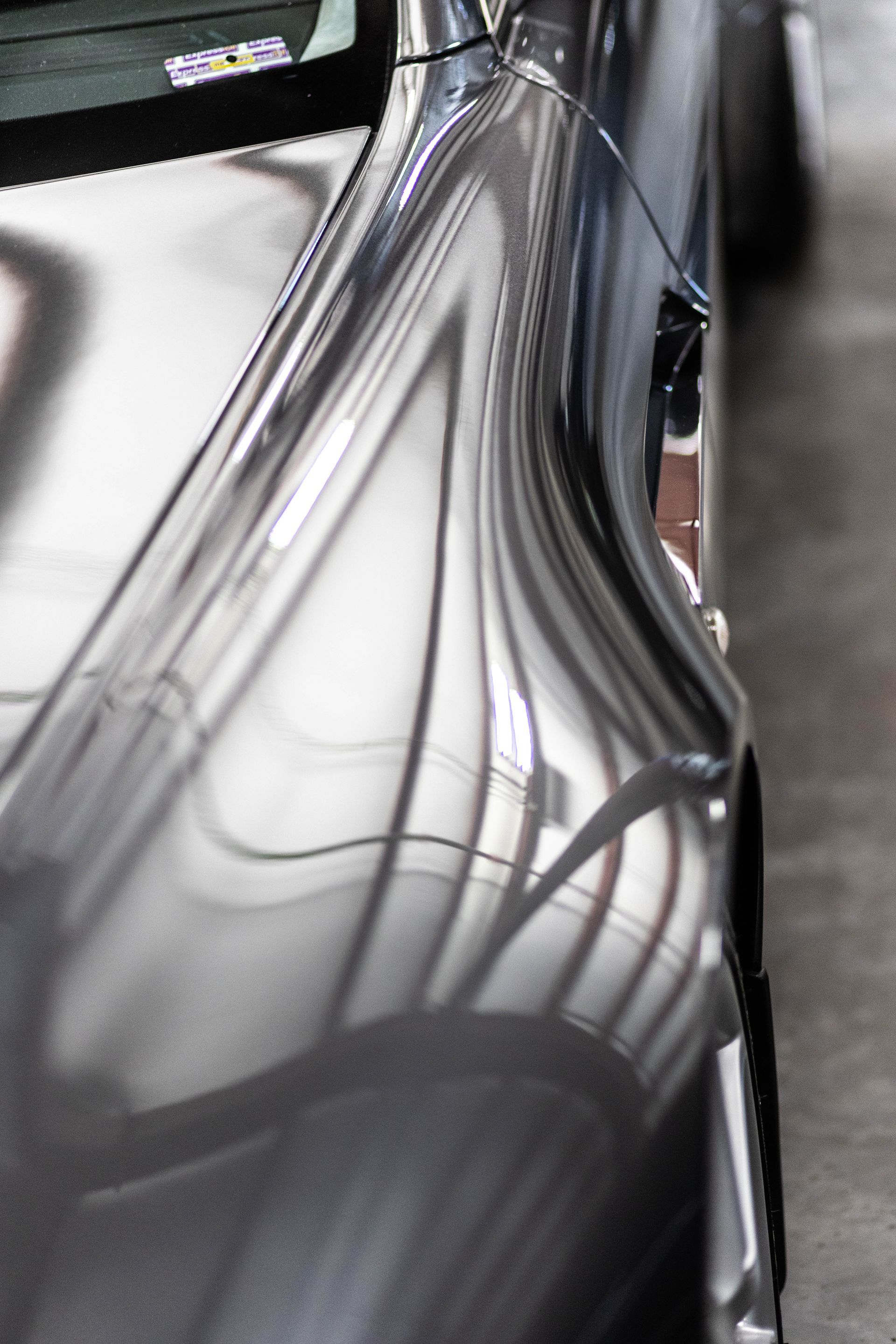 Close-up of a shiny metallic car body reflecting overhead lights and surroundings.