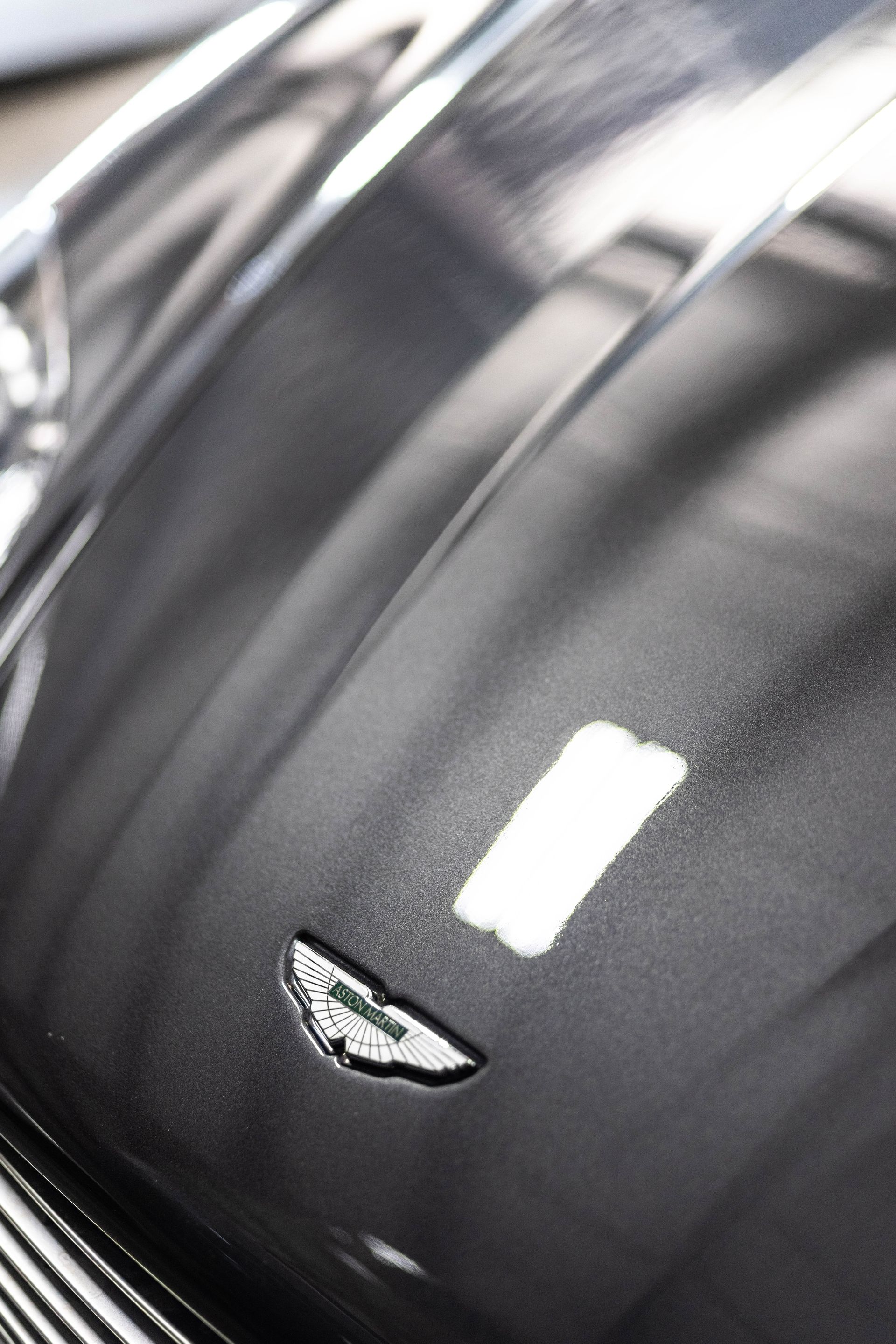 Close-up of a black Aston Martin hood with the winged emblem and light reflections