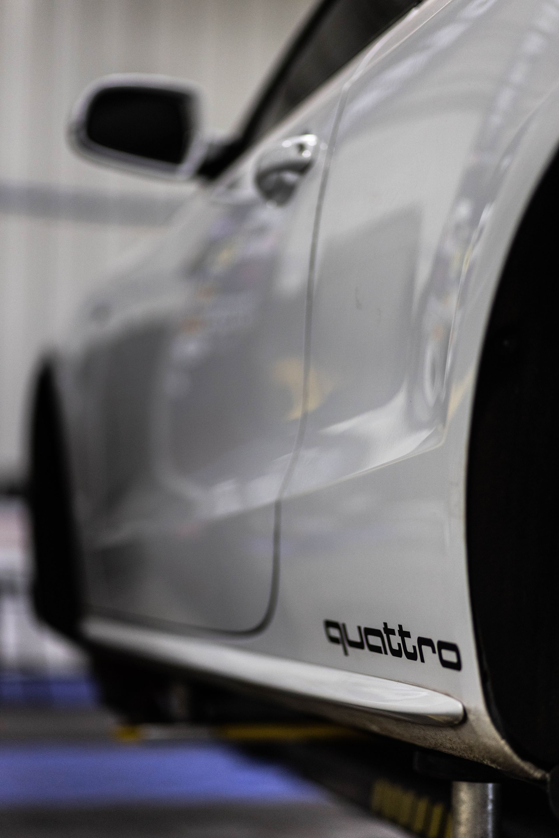 Close-up of a silver sports car side panel with a black side mirror and “quattro” badge.