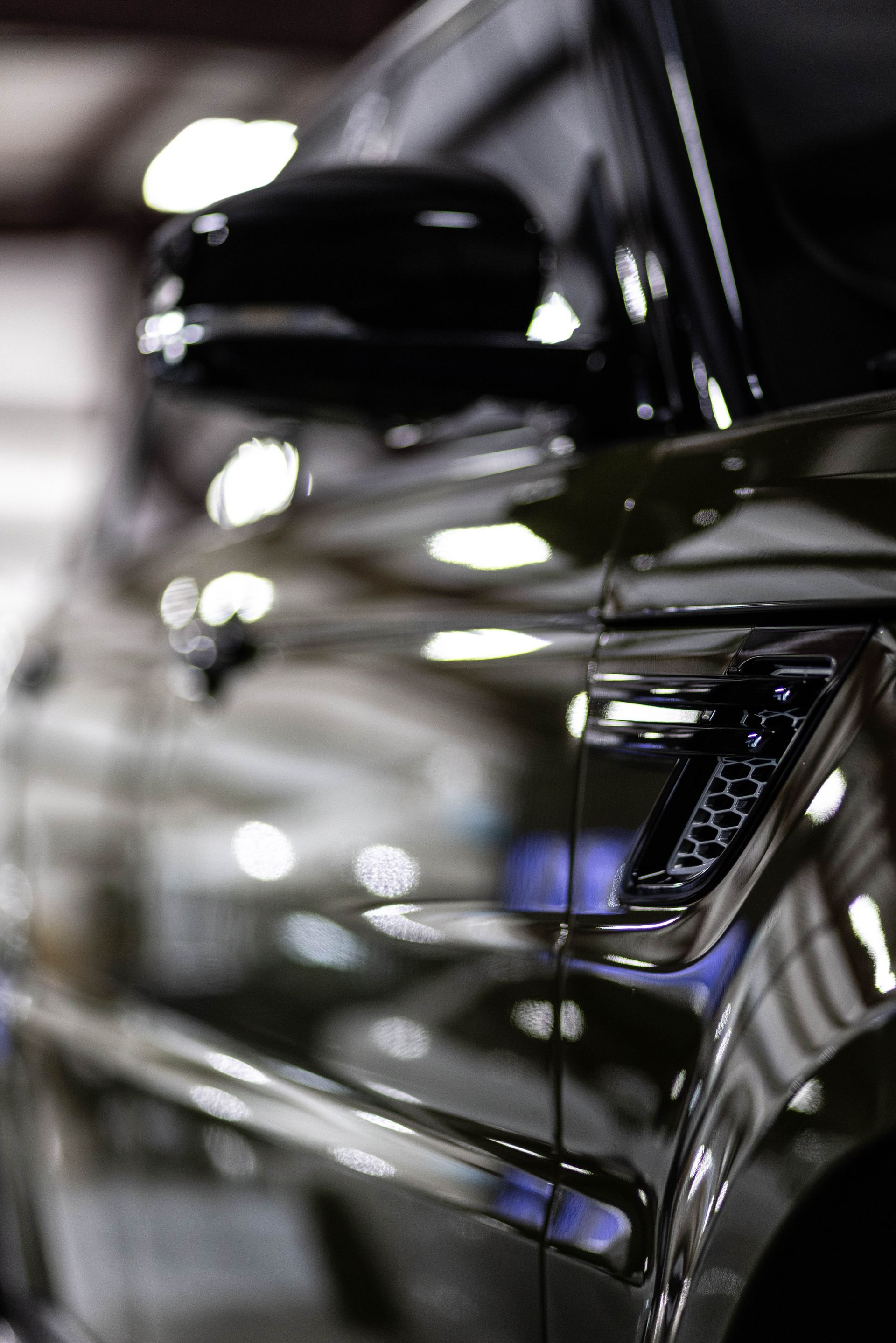 Close-up of a black car’s side mirror and chrome door handle in a glossy showroom setting