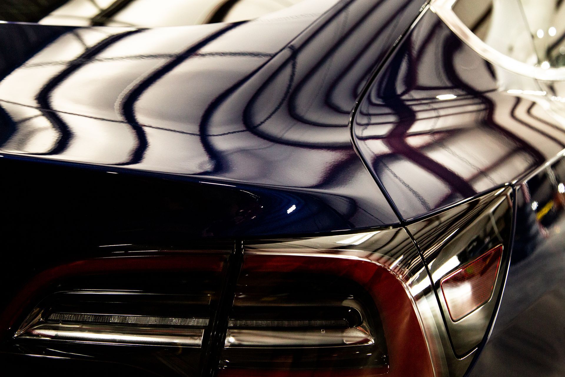 Close-up of a glossy black car trunk and taillight with abstract striped reflections across the surface