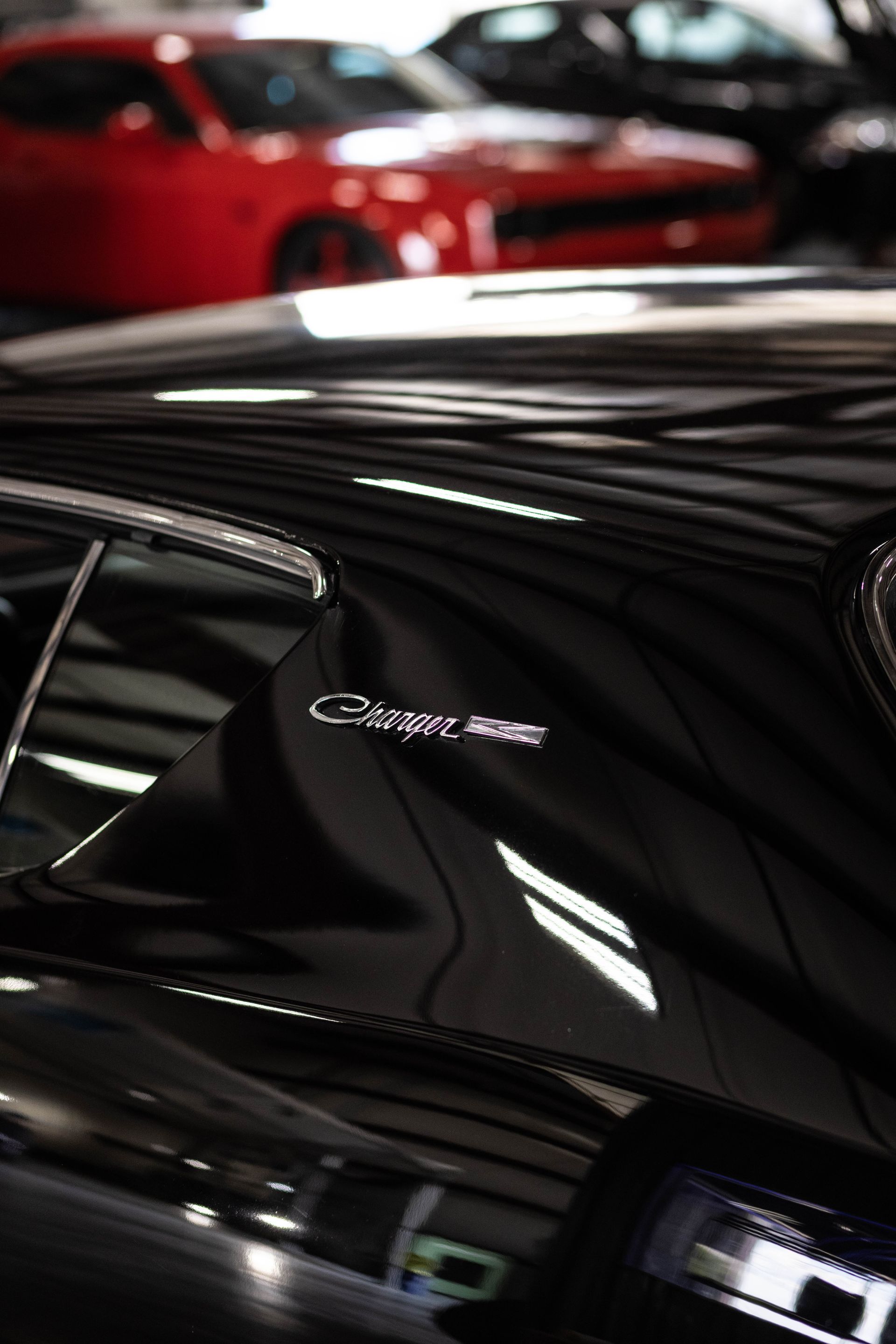 Close-up of a black Corvette emblem on a glossy sports car, with a red car blurred in the background