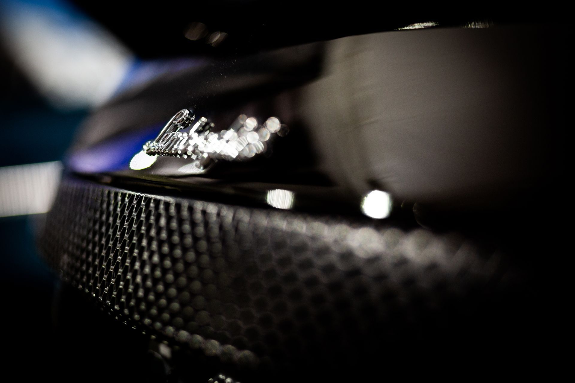 Close-up of a black car grille with a shiny emblem and blurred blue highlights