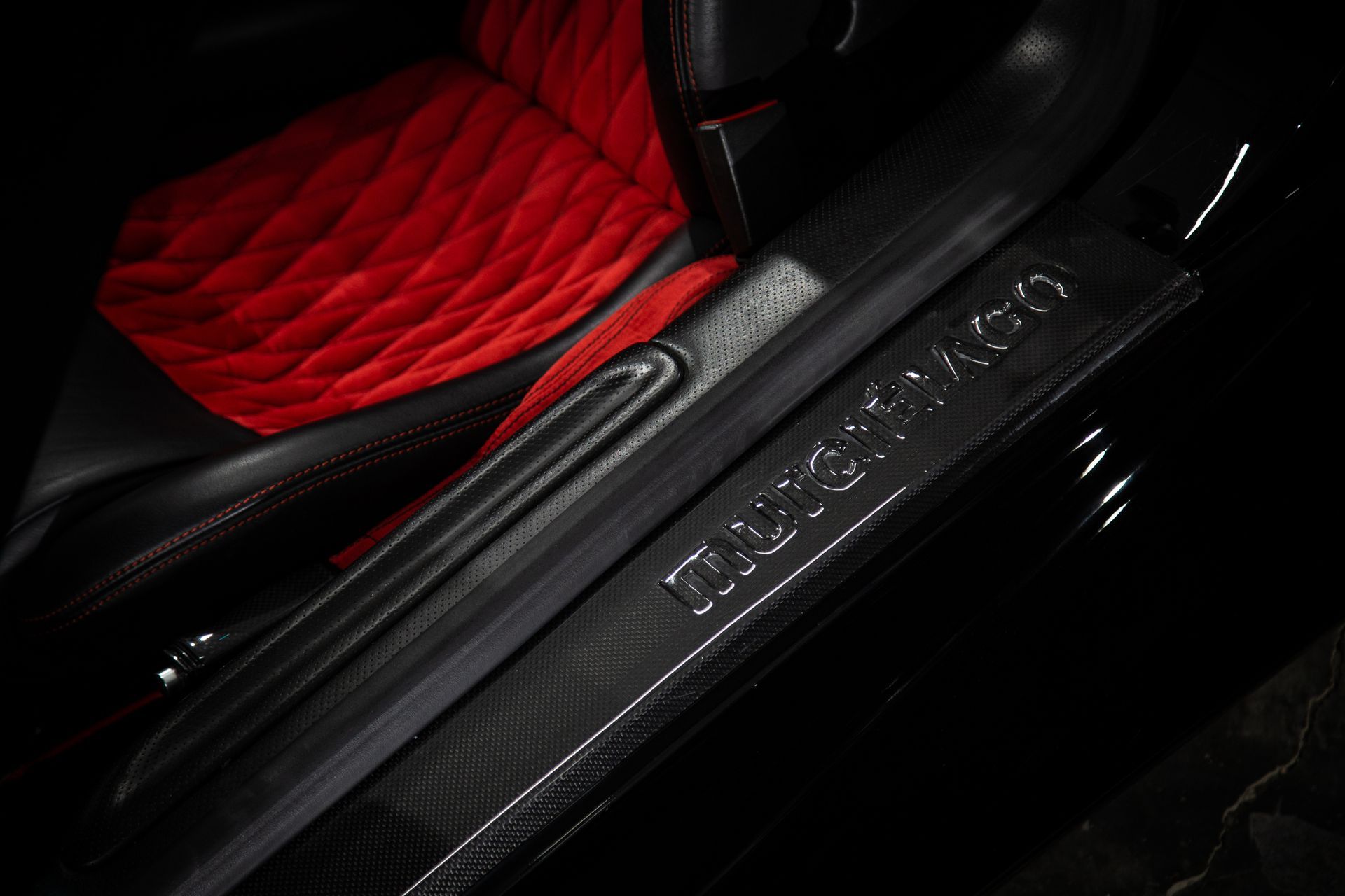 Red quilted car seat and black door sill with illuminated “AMG” trim in a dark interior
