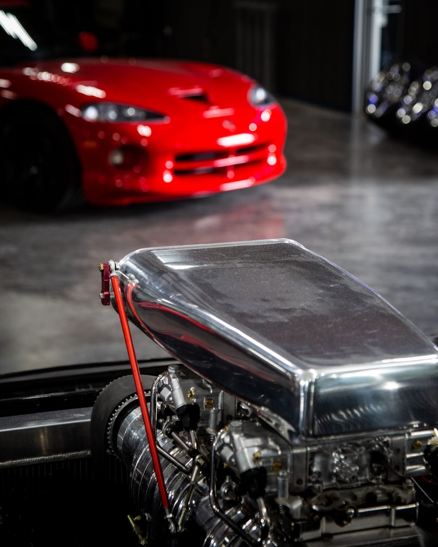 Red sports car in the background behind a chrome engine in the foreground