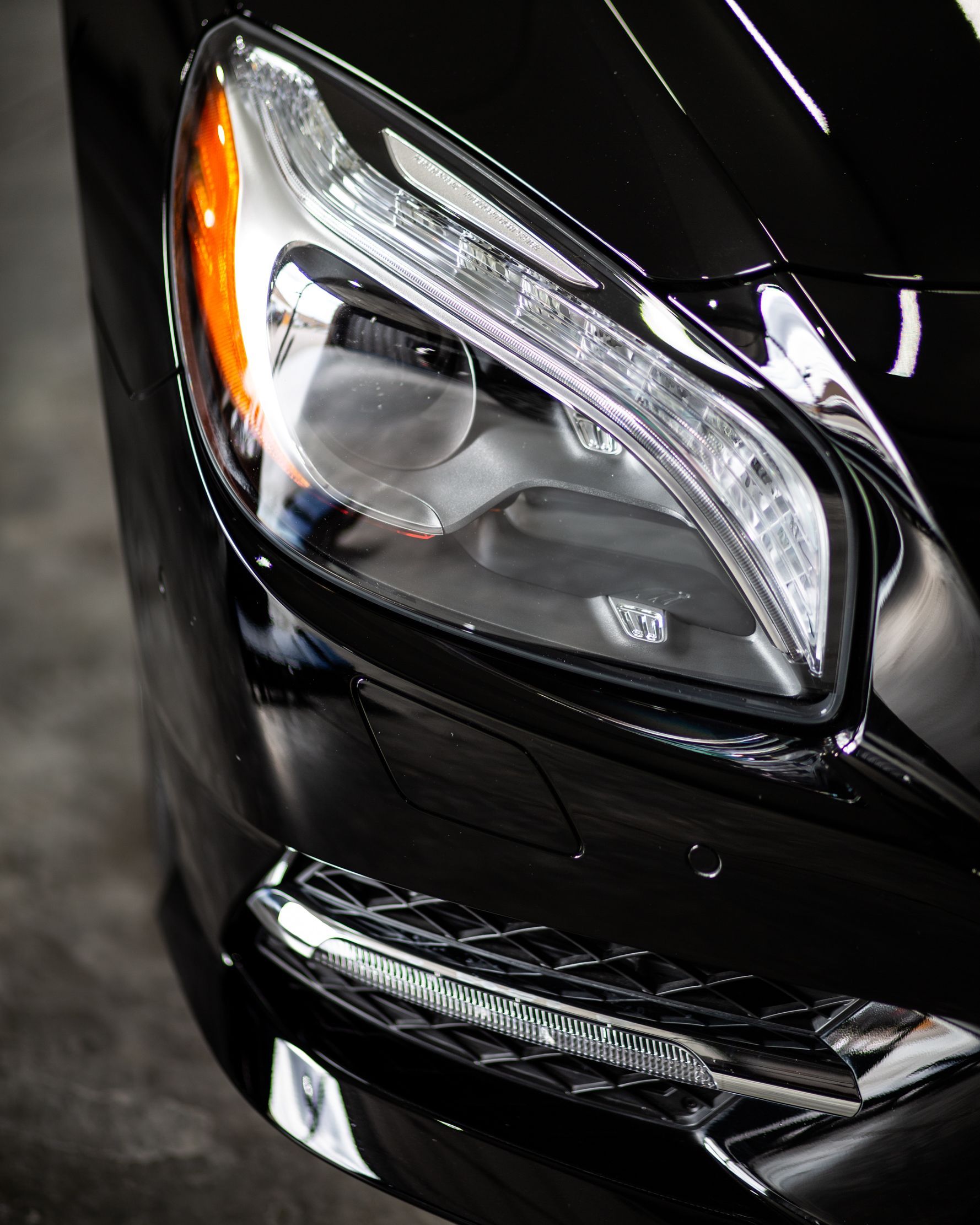 Close-up of a black car headlight with chrome details and amber side marker