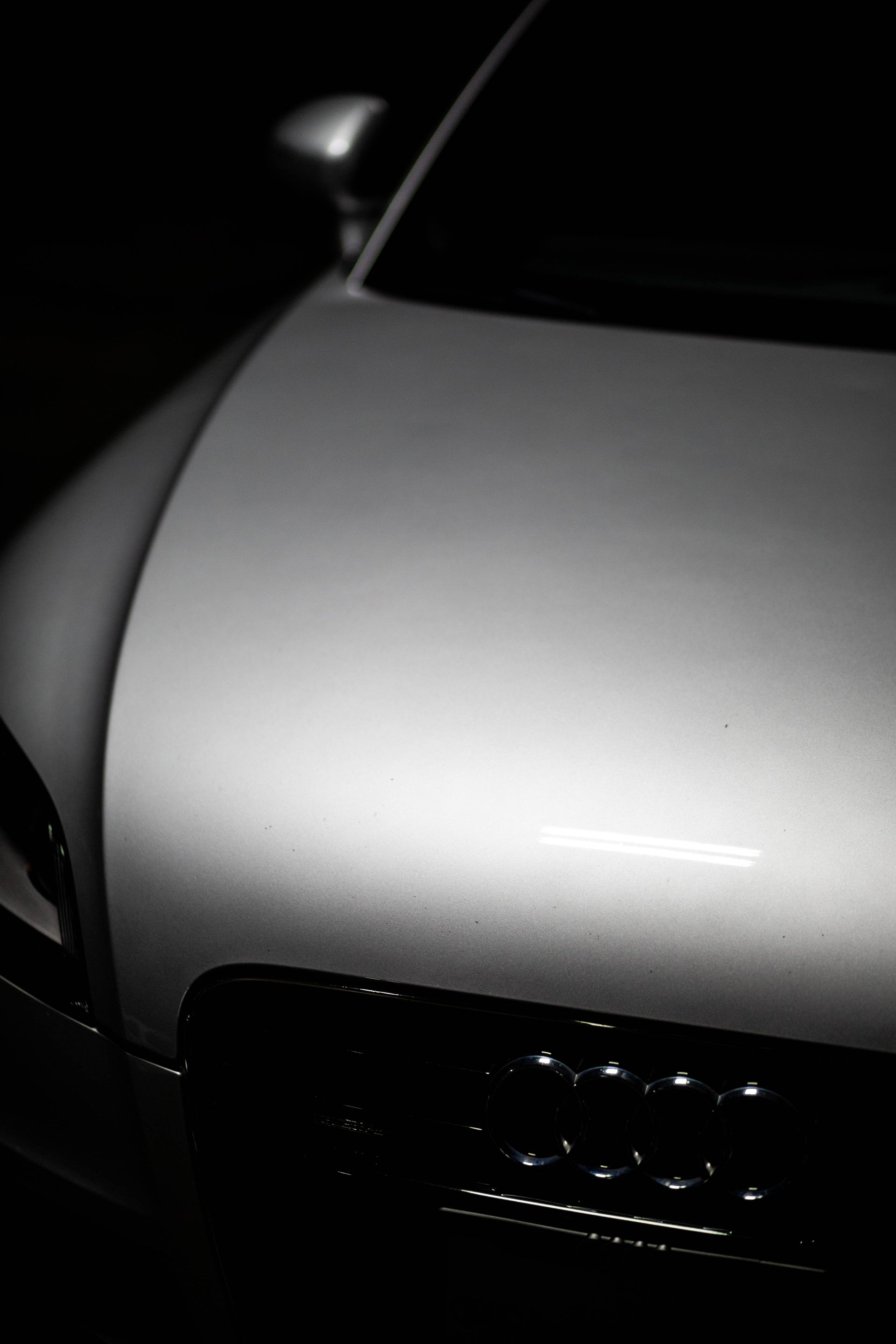 Close-up of a white car hood and front grille in dim lighting
