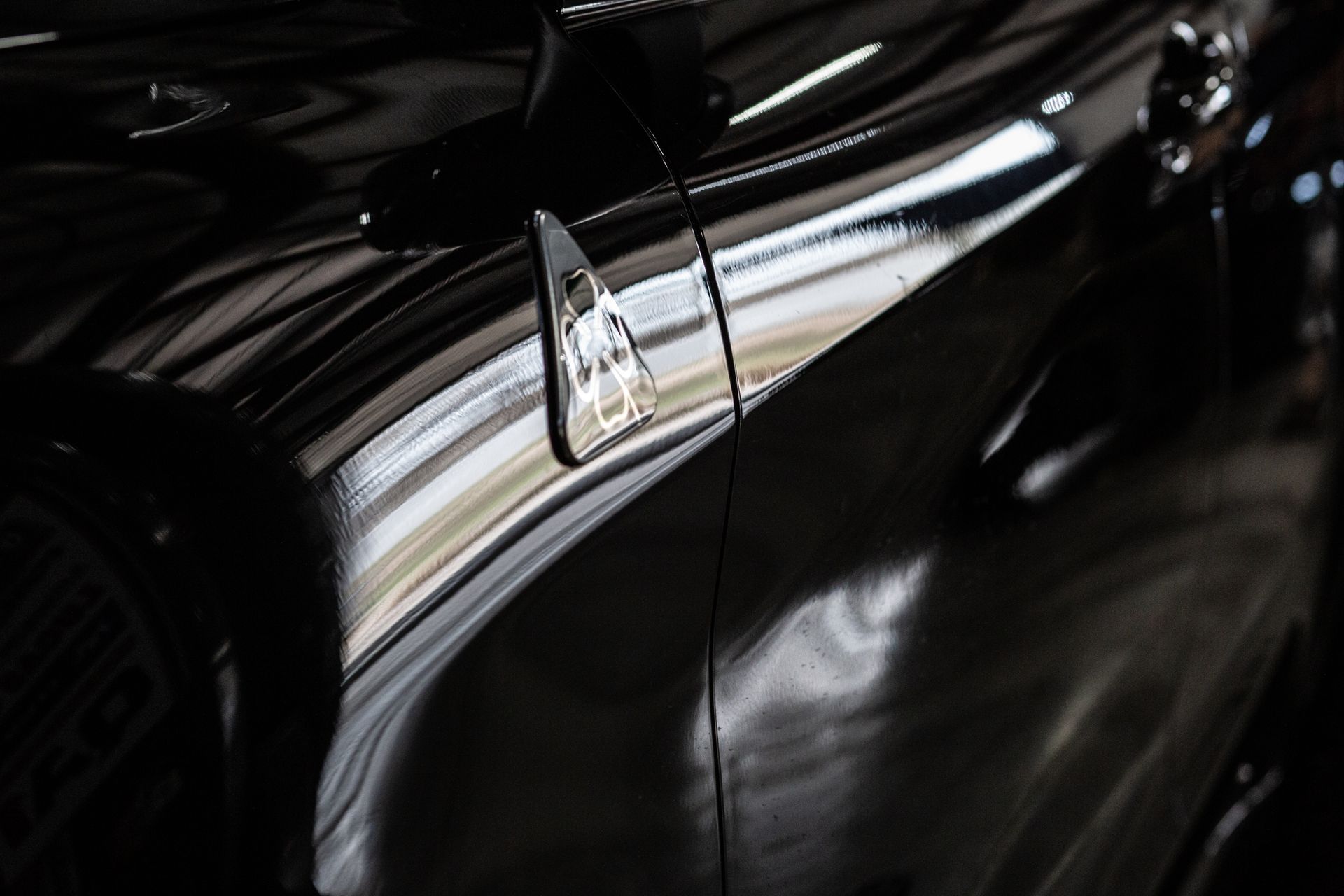 Close-up of a black car’s glossy side panel and chrome trim reflecting light