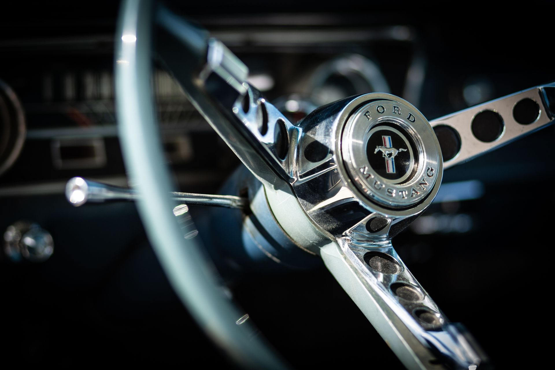 Close-up of a classic car steering wheel with chrome spokes and a Mustang emblem