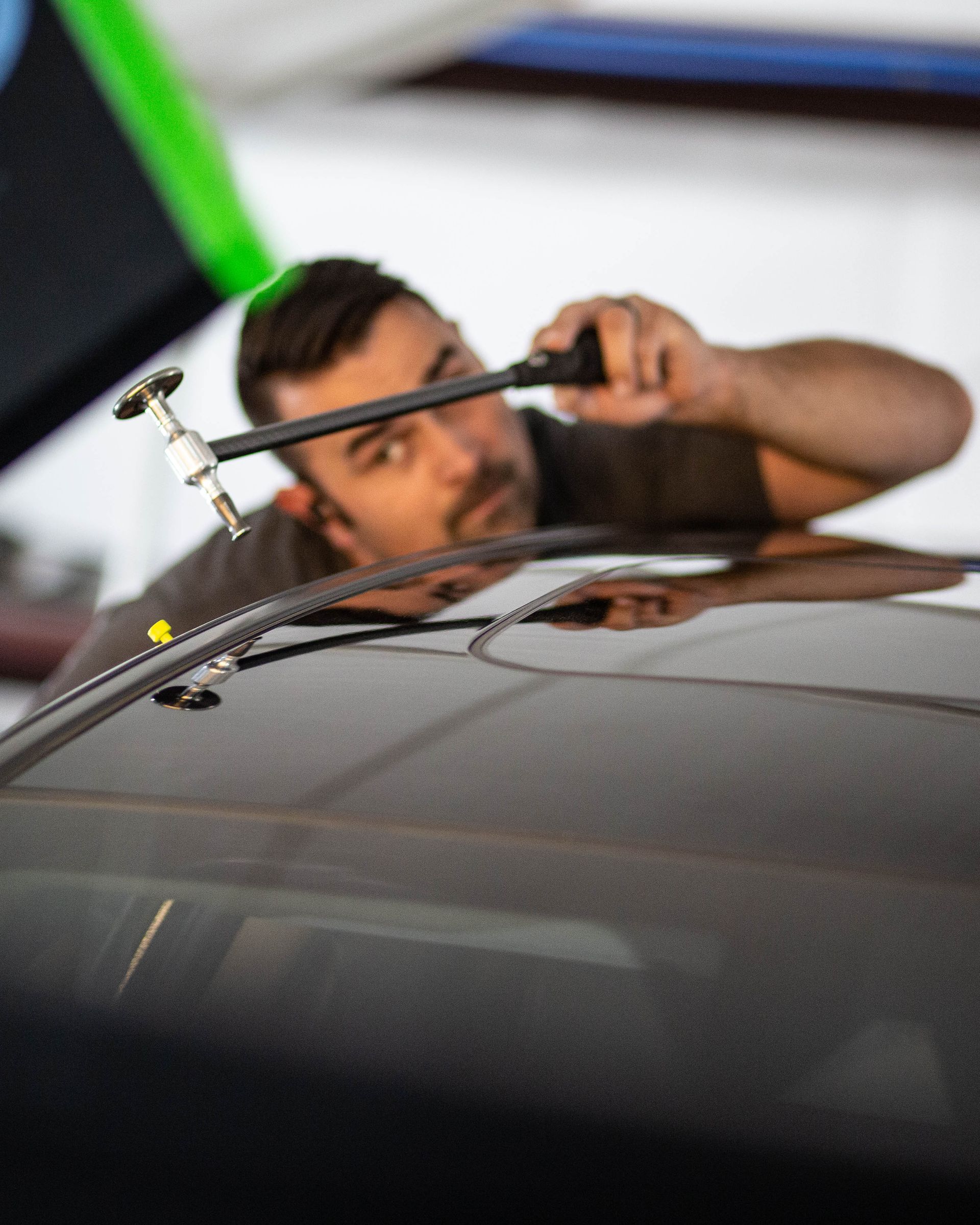 Mechanic using a tool on a car roof in a garage, with blurred green and blue background lines