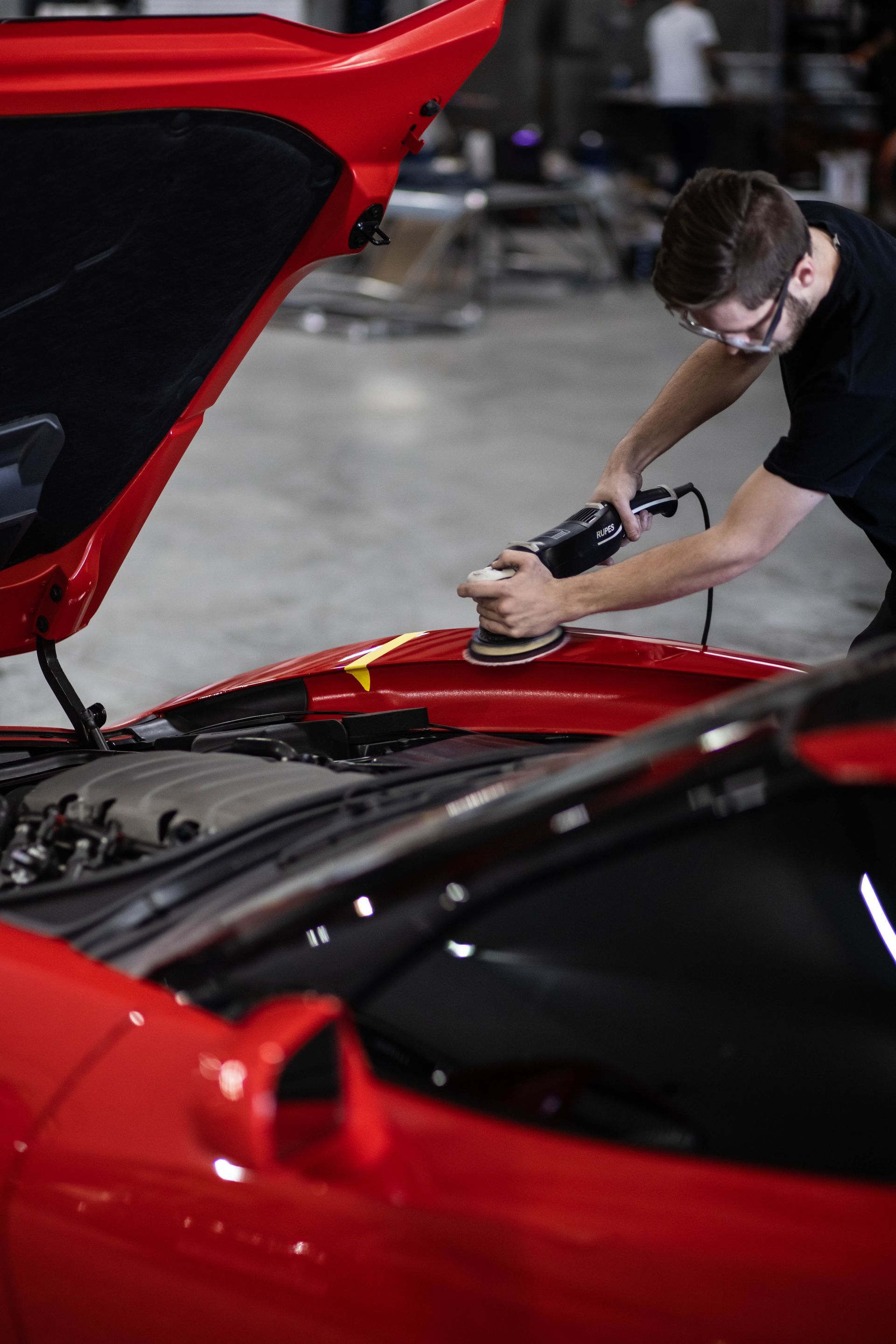 Mechanic polishing a red sports car in a garage with the hood open