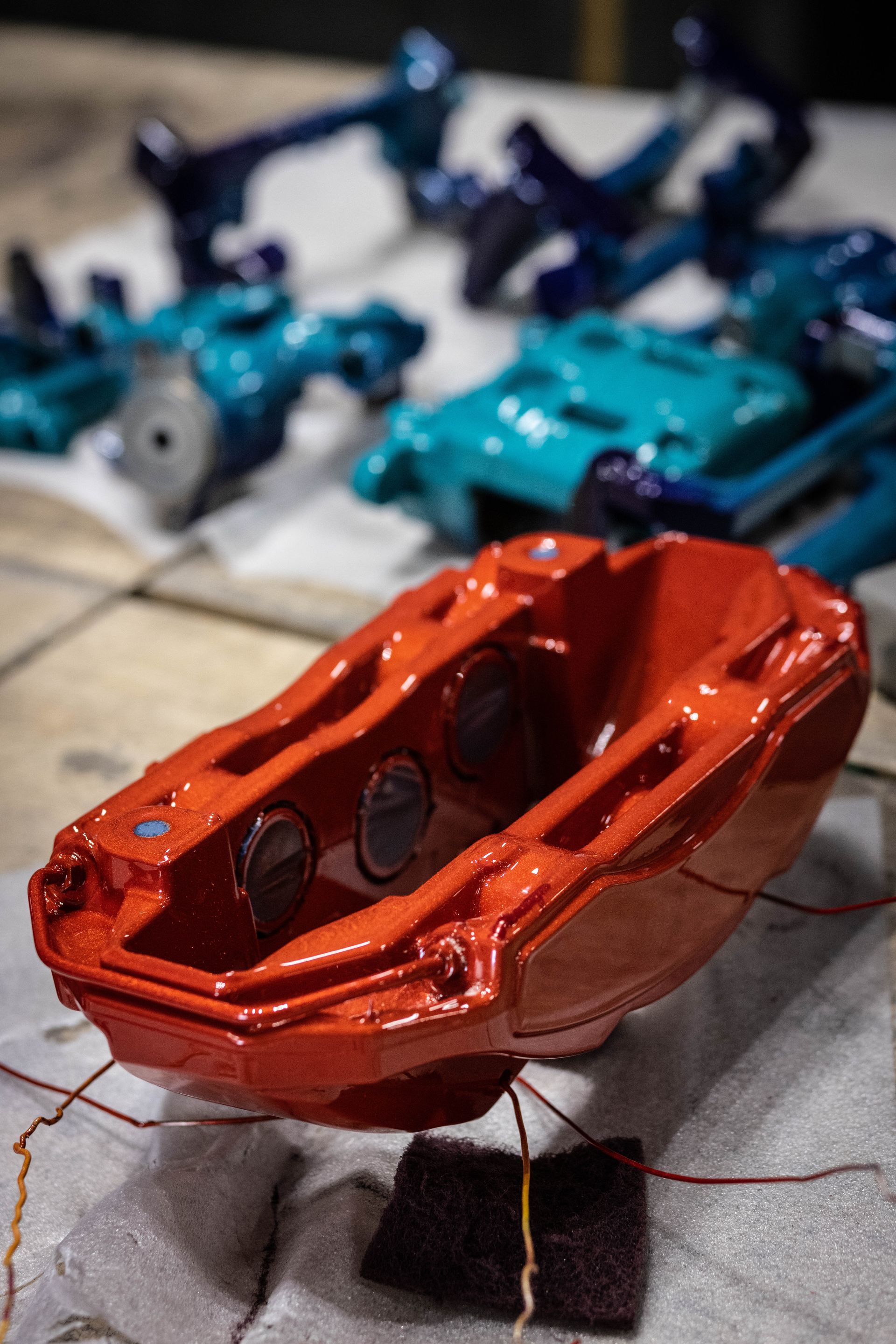 Orange car body shell in the foreground with several blue model car parts blurred behind it on a work surface