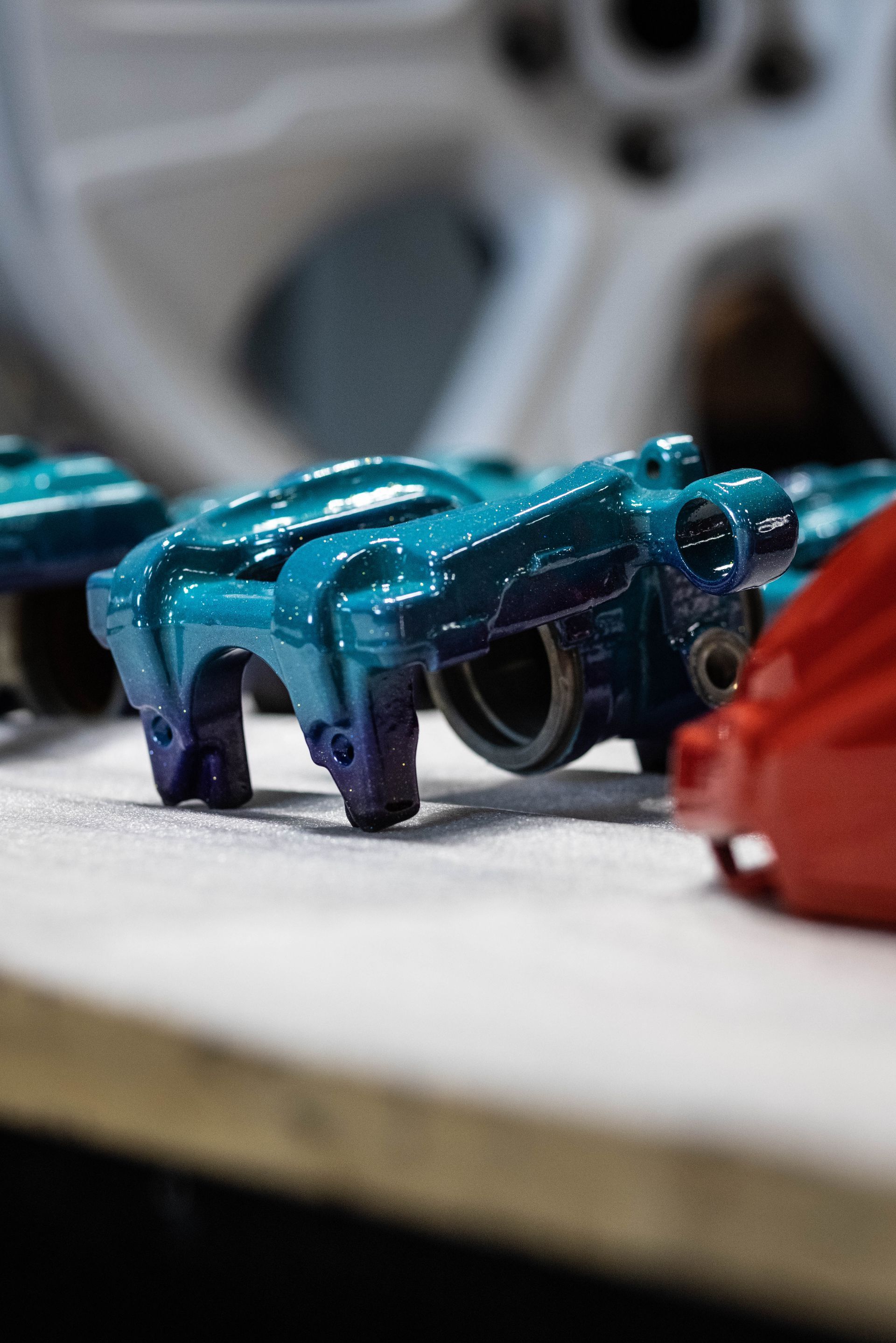 Blue toy race car on a table, with a blurred wheel in the background and a red object in the foreground