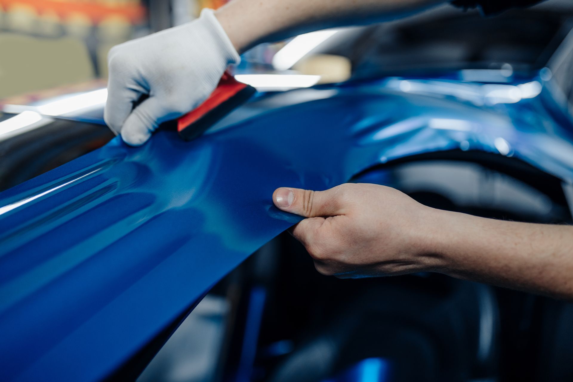 Hands applying blue protective film to a car body panel in a workshop