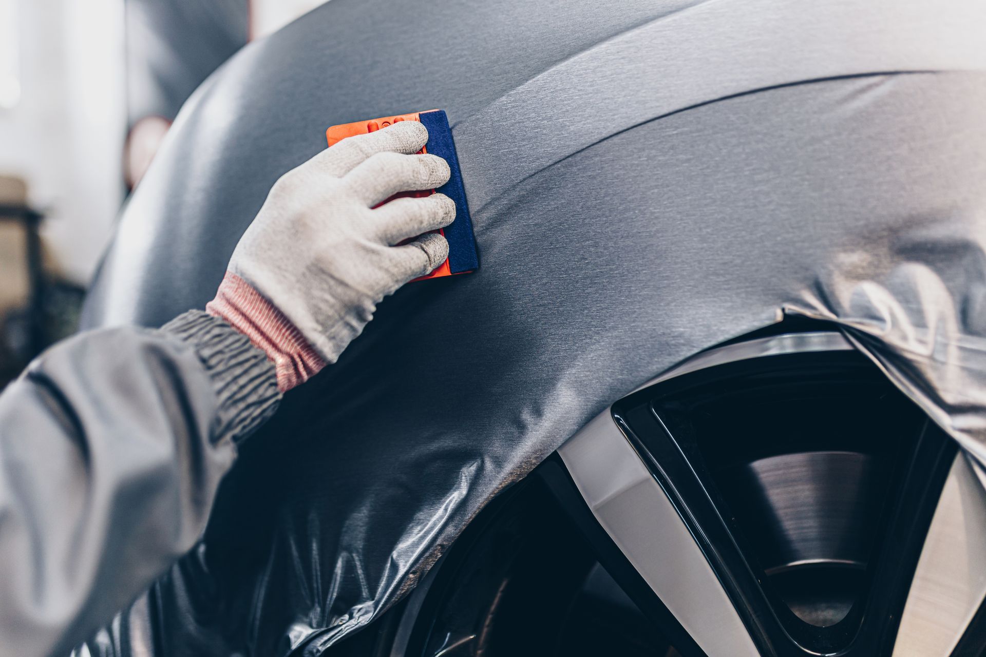 Gloved hand wiping a gray car hood with a cloth near the windshield