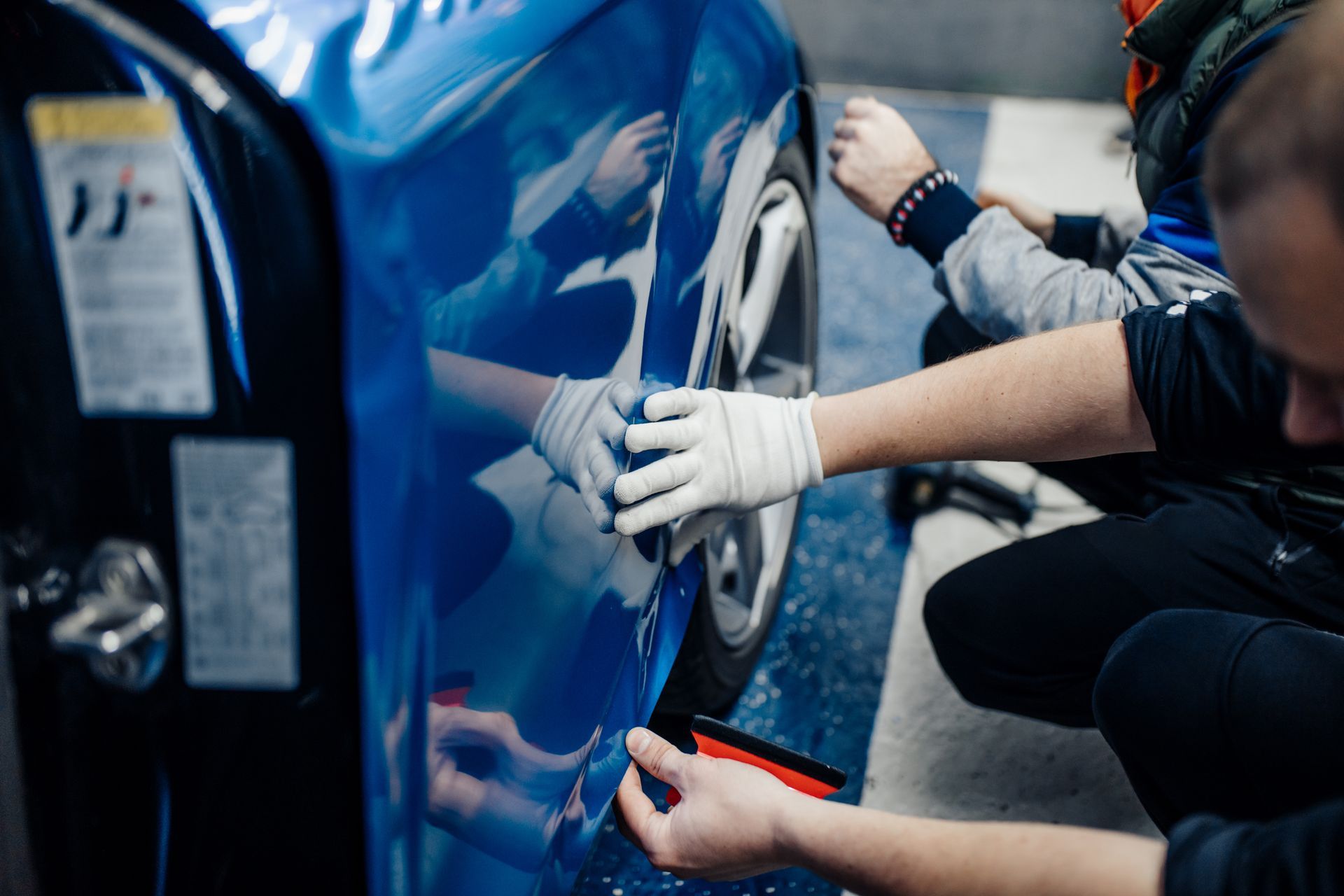 People wearing white gloves polishing a blue car door in a garage