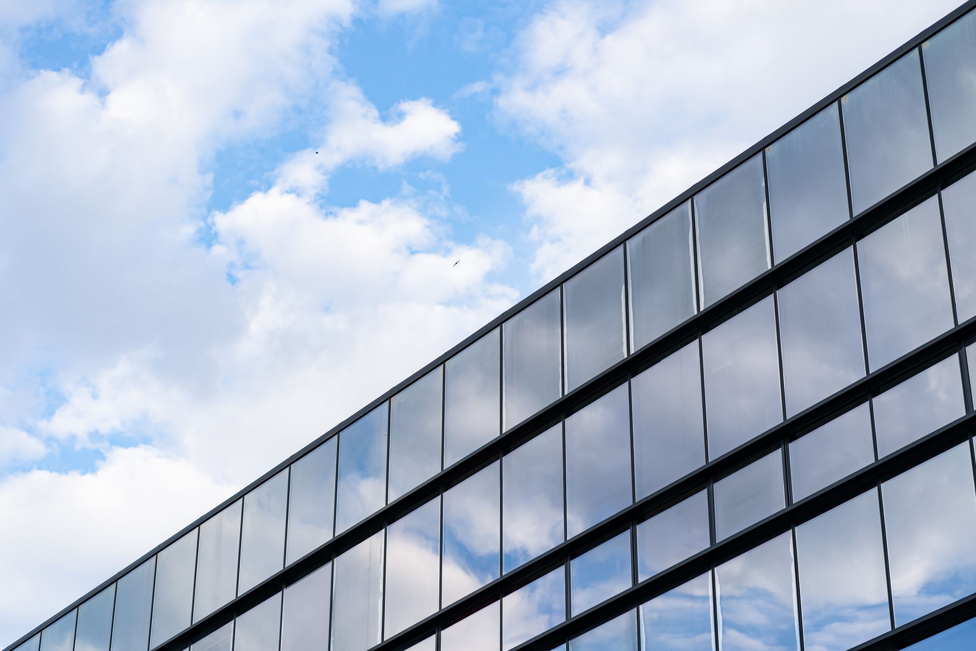 Modern glass office building reflecting clouds and blue sky