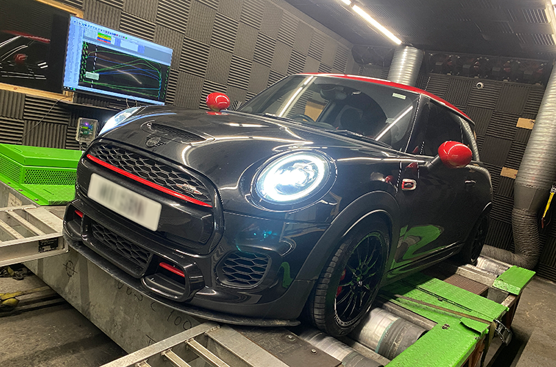 A black mini cooper jcw is being tested on a dyno in a garage.
