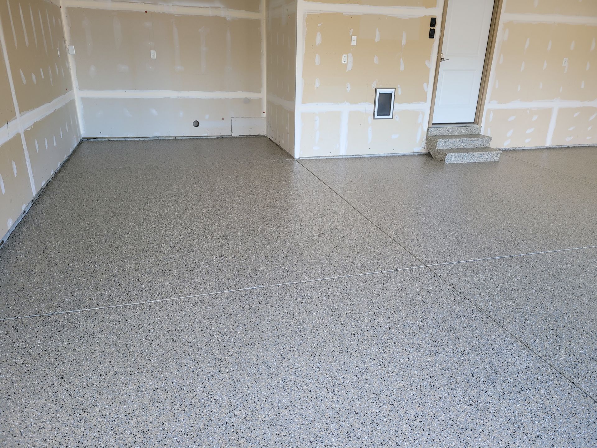 Garage with a speckled epoxy floor; tan walls, white door and steps.