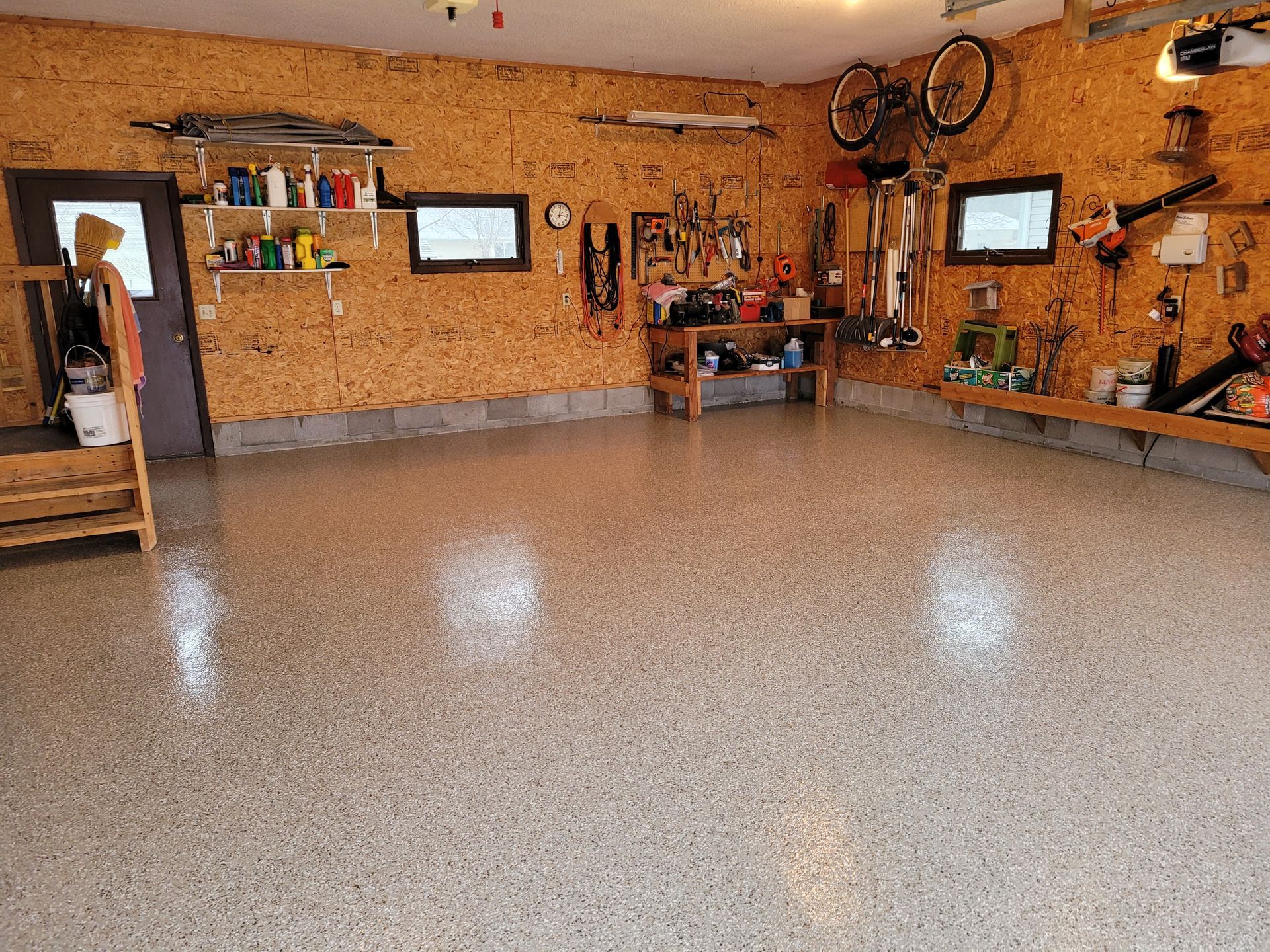 Garage interior with a shiny, speckled epoxy floor, tools, and storage on the walls.