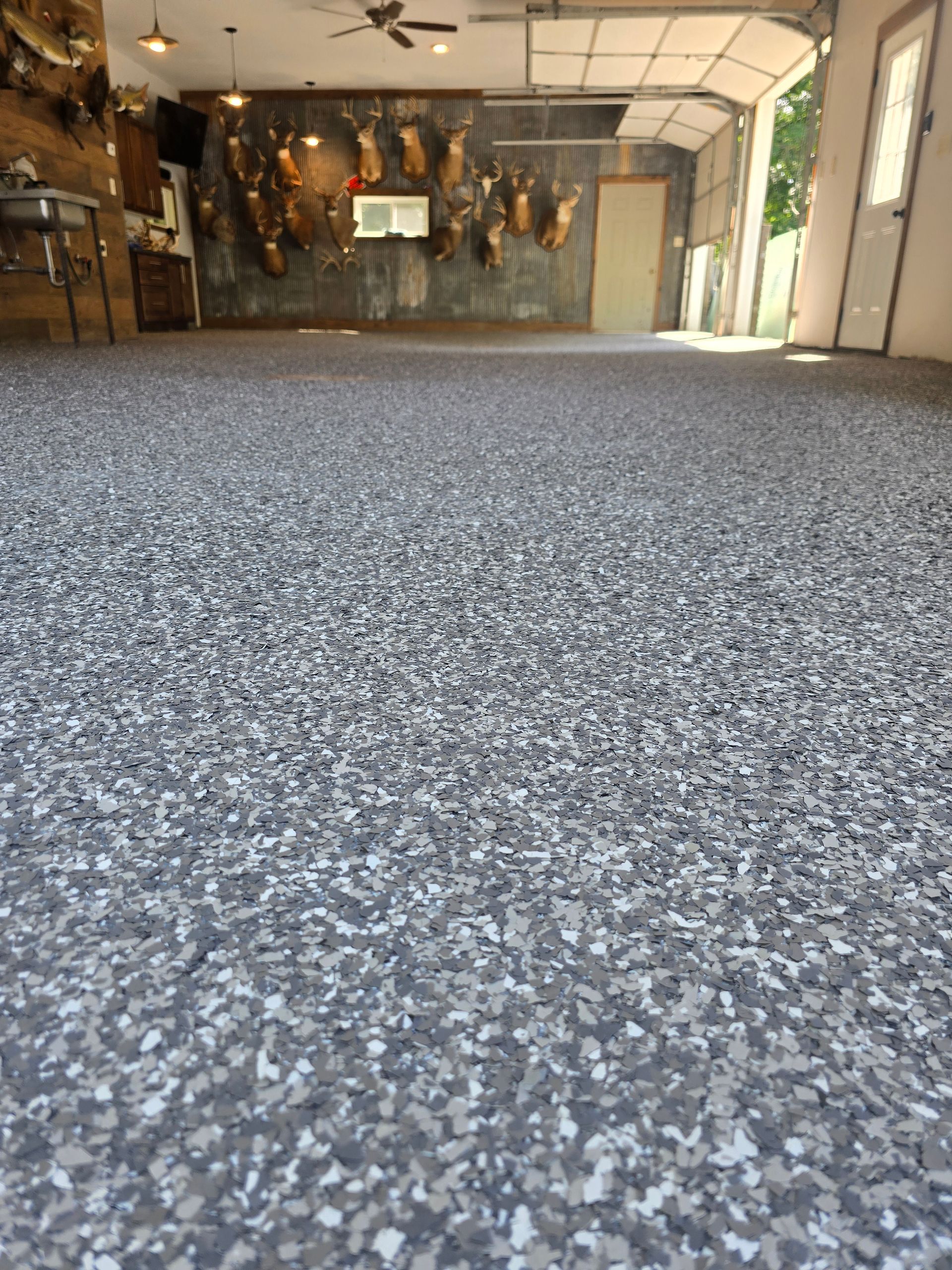 Granite-like epoxy floor in a garage with open door, showing an interior, dimly lit space with mounted animal heads.