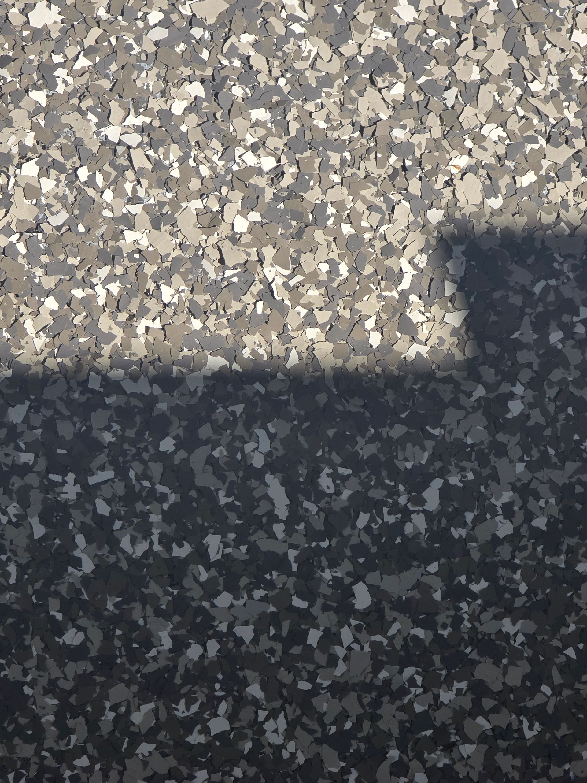Close-up of a speckled, gray floor with a dark shadow cast across the lower half.
