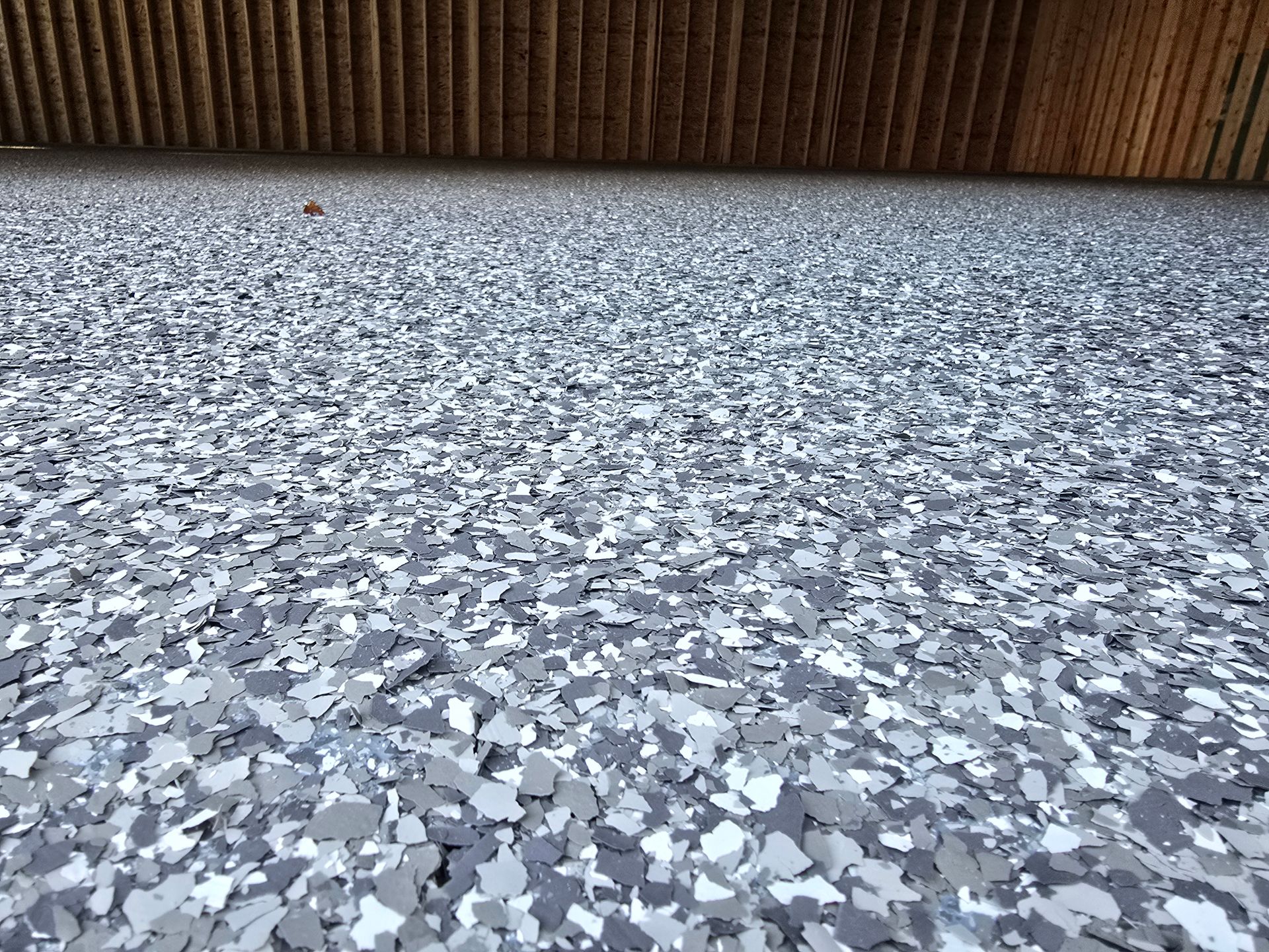 Gray and white speckled flooring under a brown wooden wall.