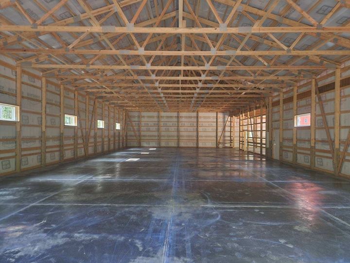 Interior view of a large, empty pole barn with a concrete floor and wooden beams.