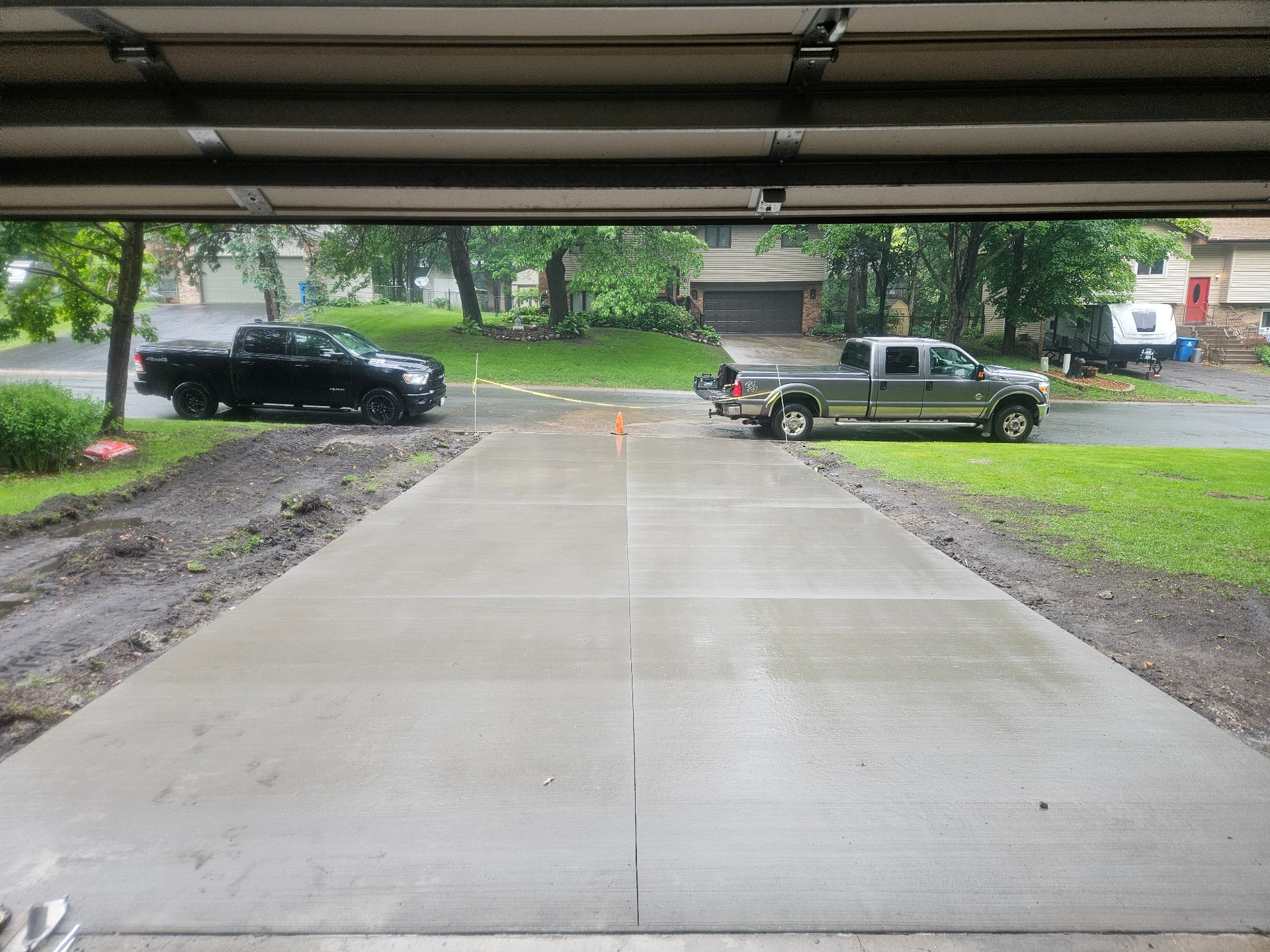 Newly poured concrete driveway with two trucks parked on it, viewed from inside a garage.