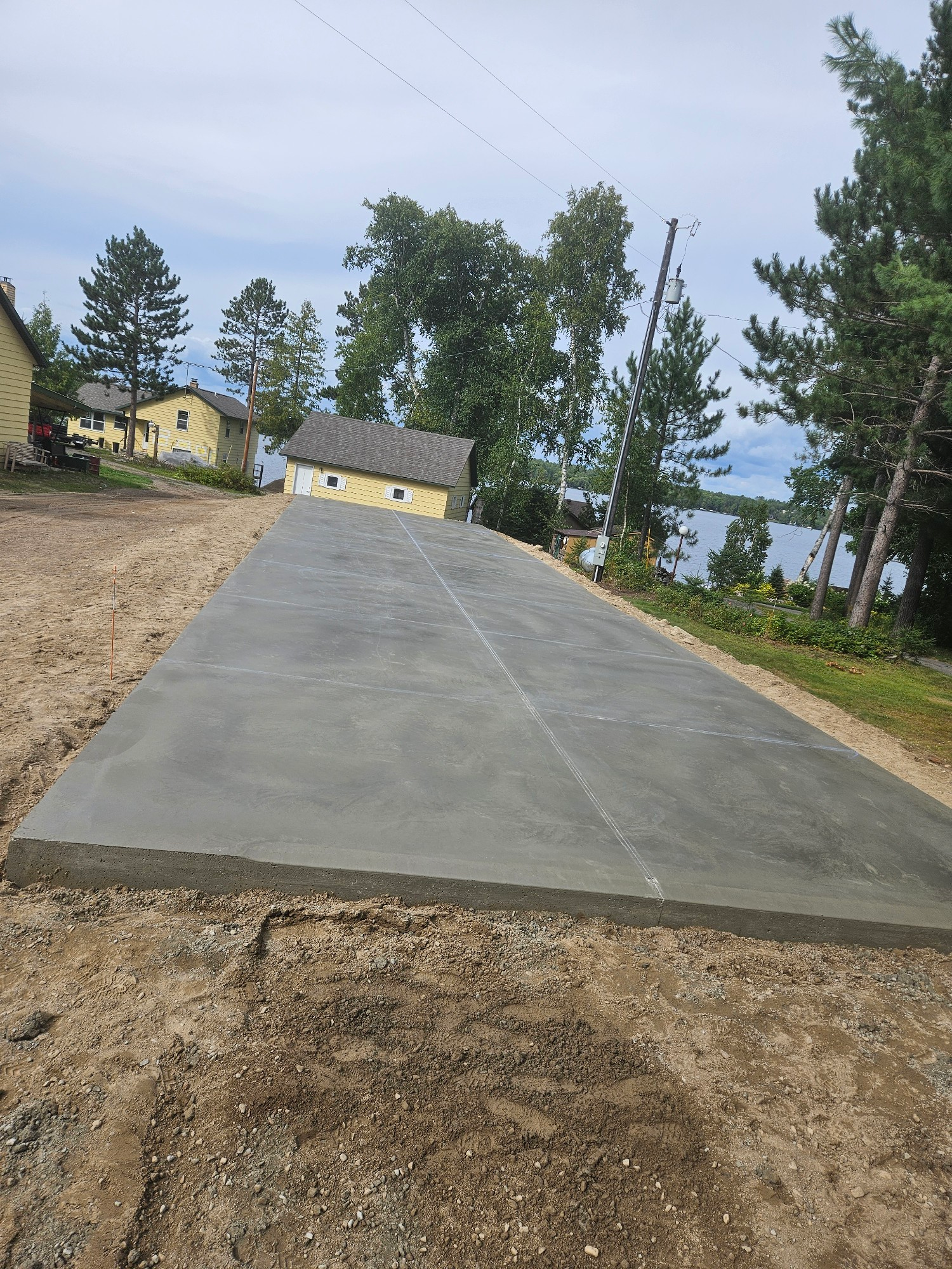 Newly poured concrete driveway leading uphill towards yellow building, overlooking water.