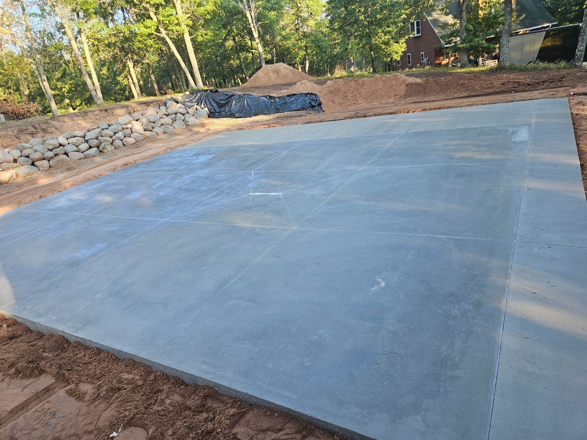 A freshly poured concrete slab in an outdoor setting, surrounded by dirt and landscaping.