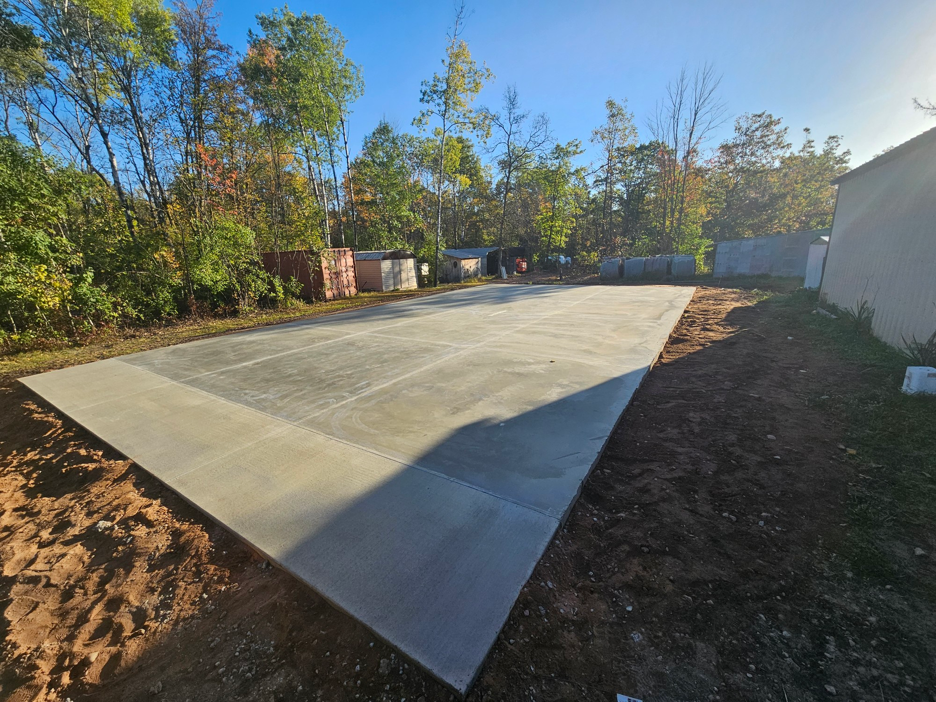 Newly poured concrete slab in an outdoor setting with trees and dirt visible.