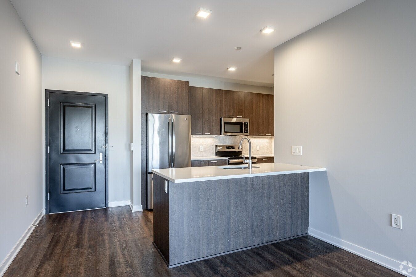 Modern kitchen with stainless steel appliances, gray island, wood floors, and black front door