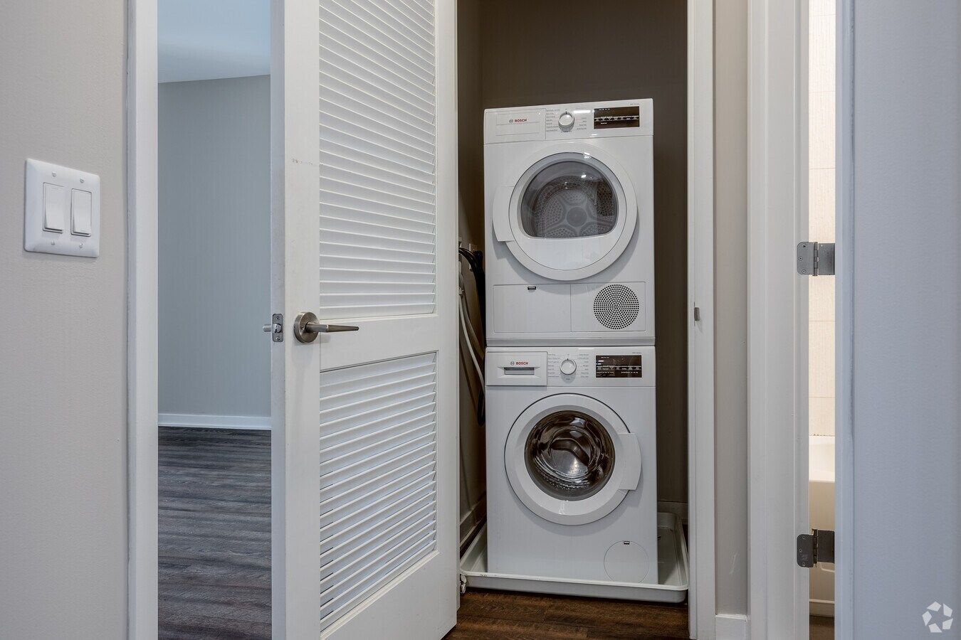 Stacked washer and dryer in a hallway closet with louvered white doors open